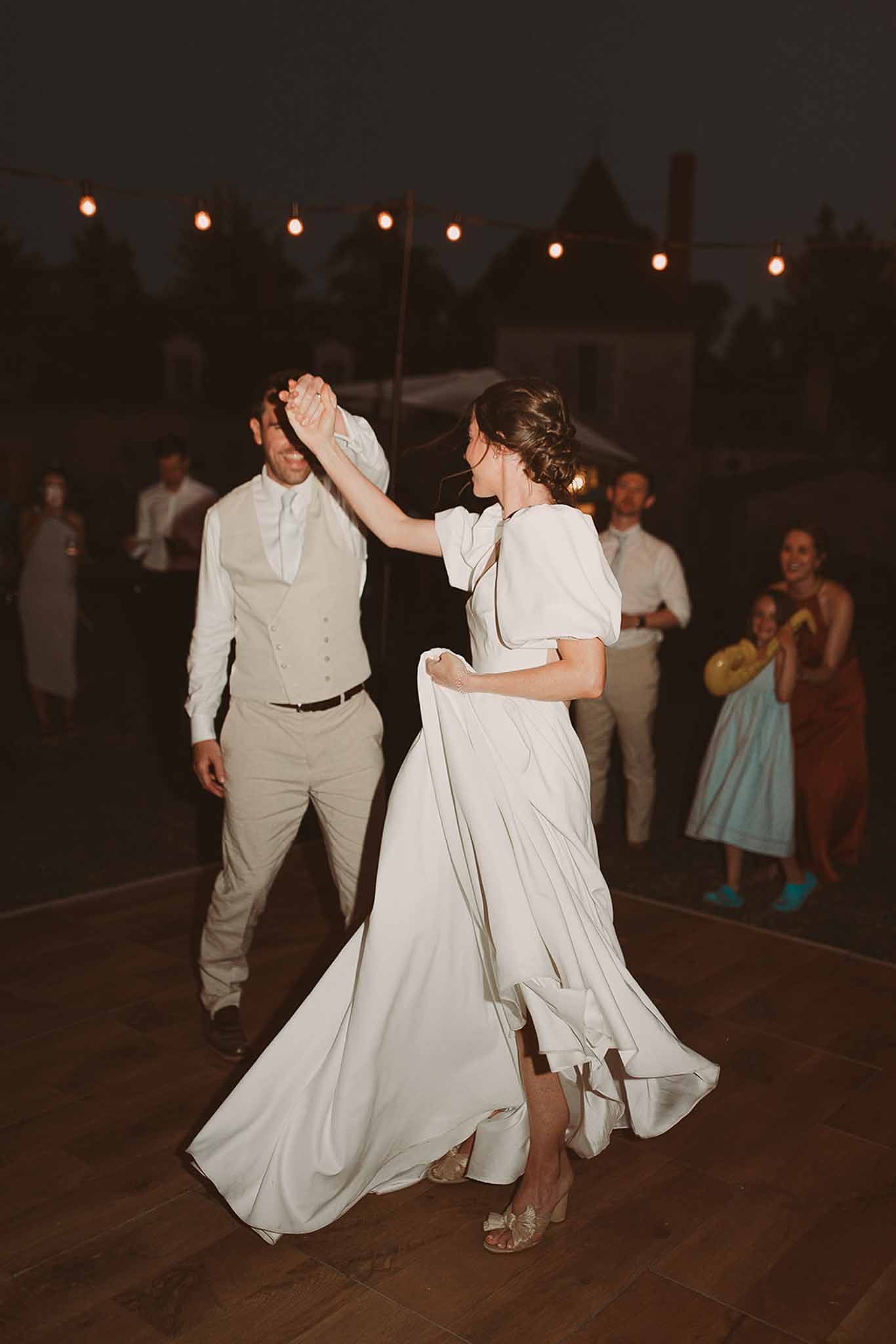 Bride and groom first dance on outdoor terrace with string lights and guests watching