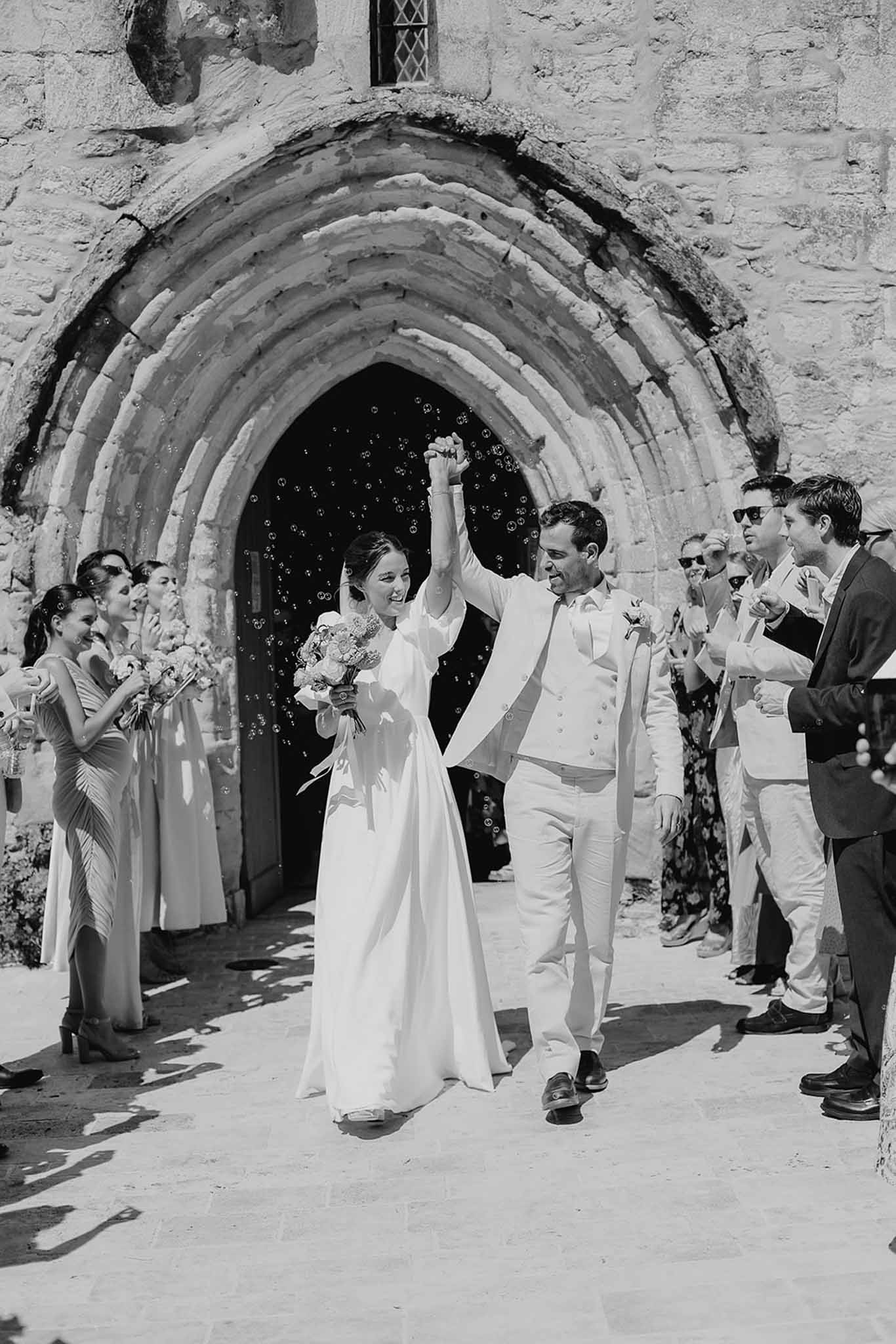 Newlywed couple exits stone chapel during wedding recessional with guests throwing confetti