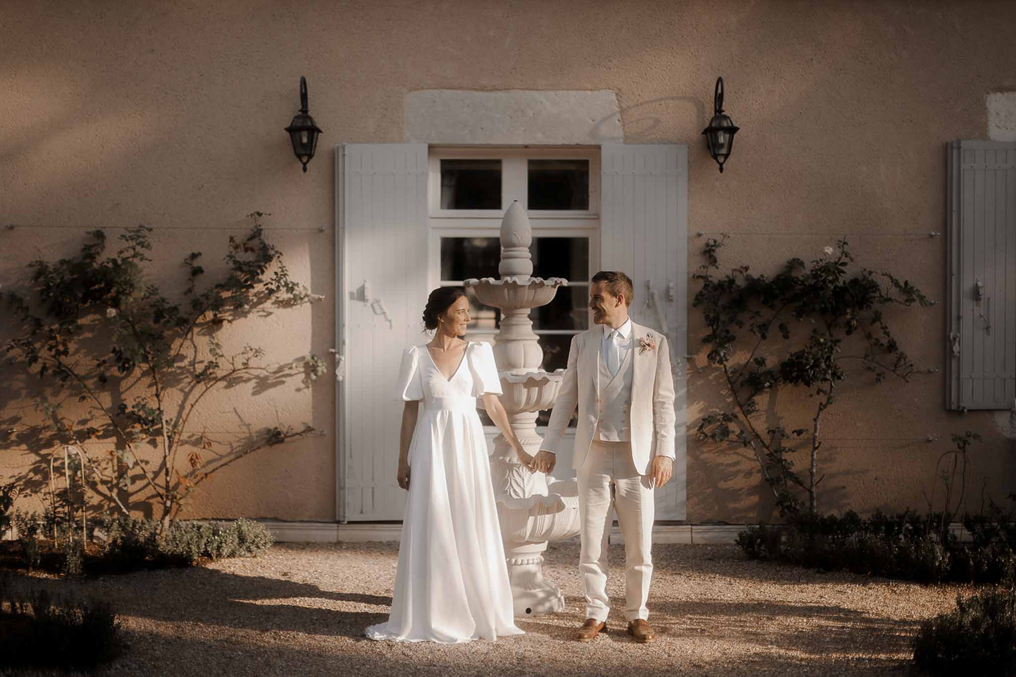 Bride and groom holding hands in classical courtyard with stone fountain and terracotta walls