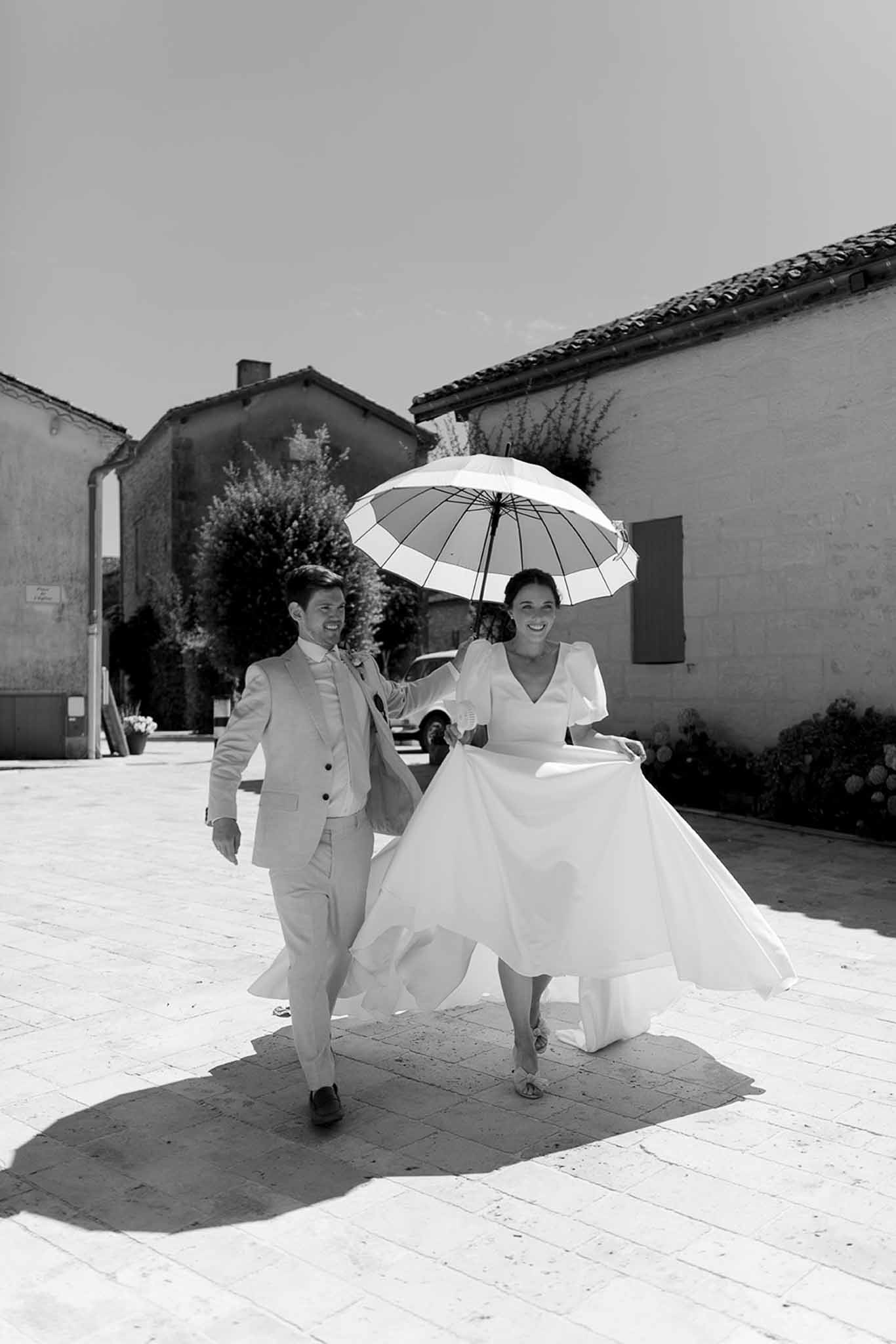Bride and groom walking with umbrella in rustic stone courtyard during light rain