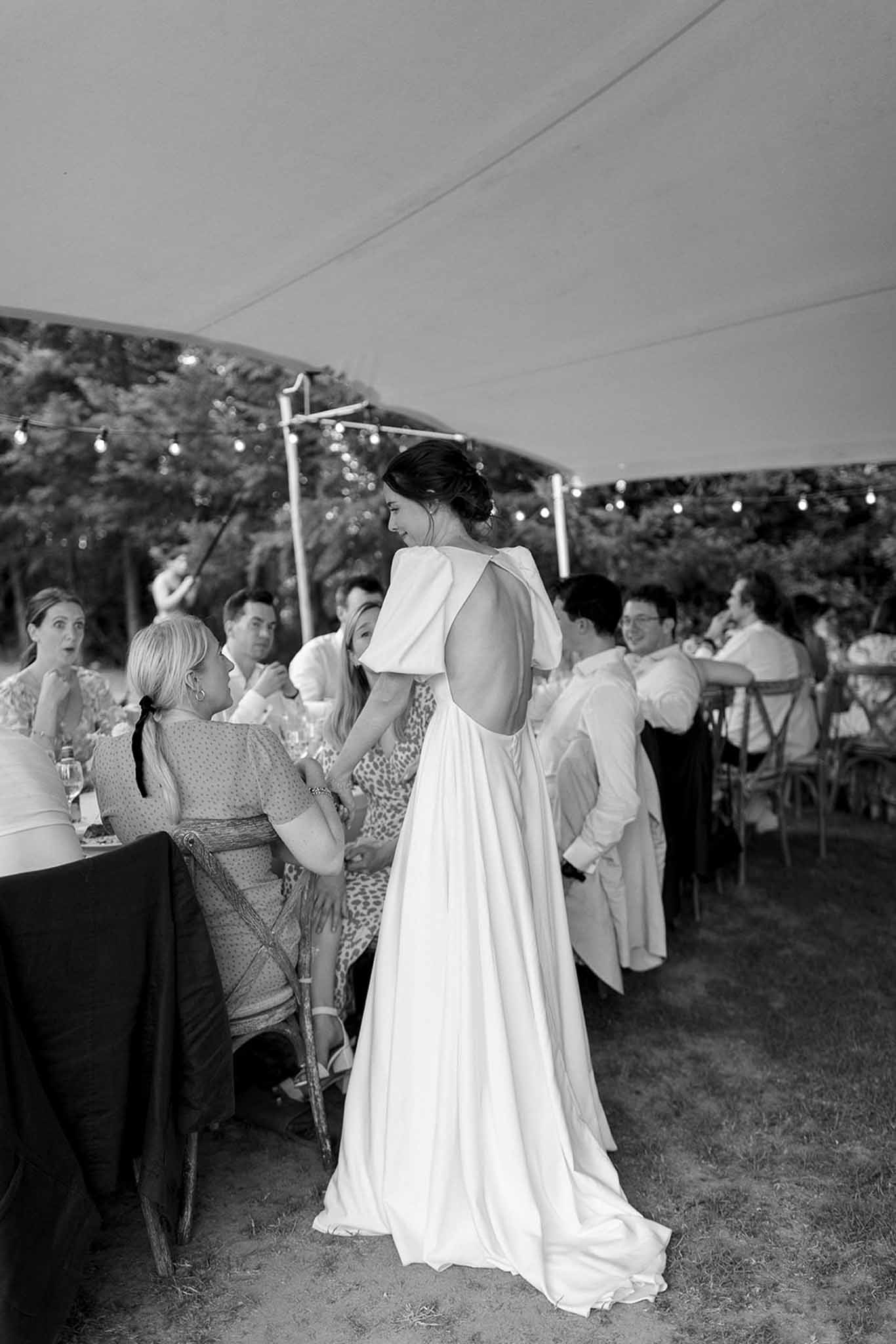 Bride in flowing gown interacting with guests at outdoor tent reception