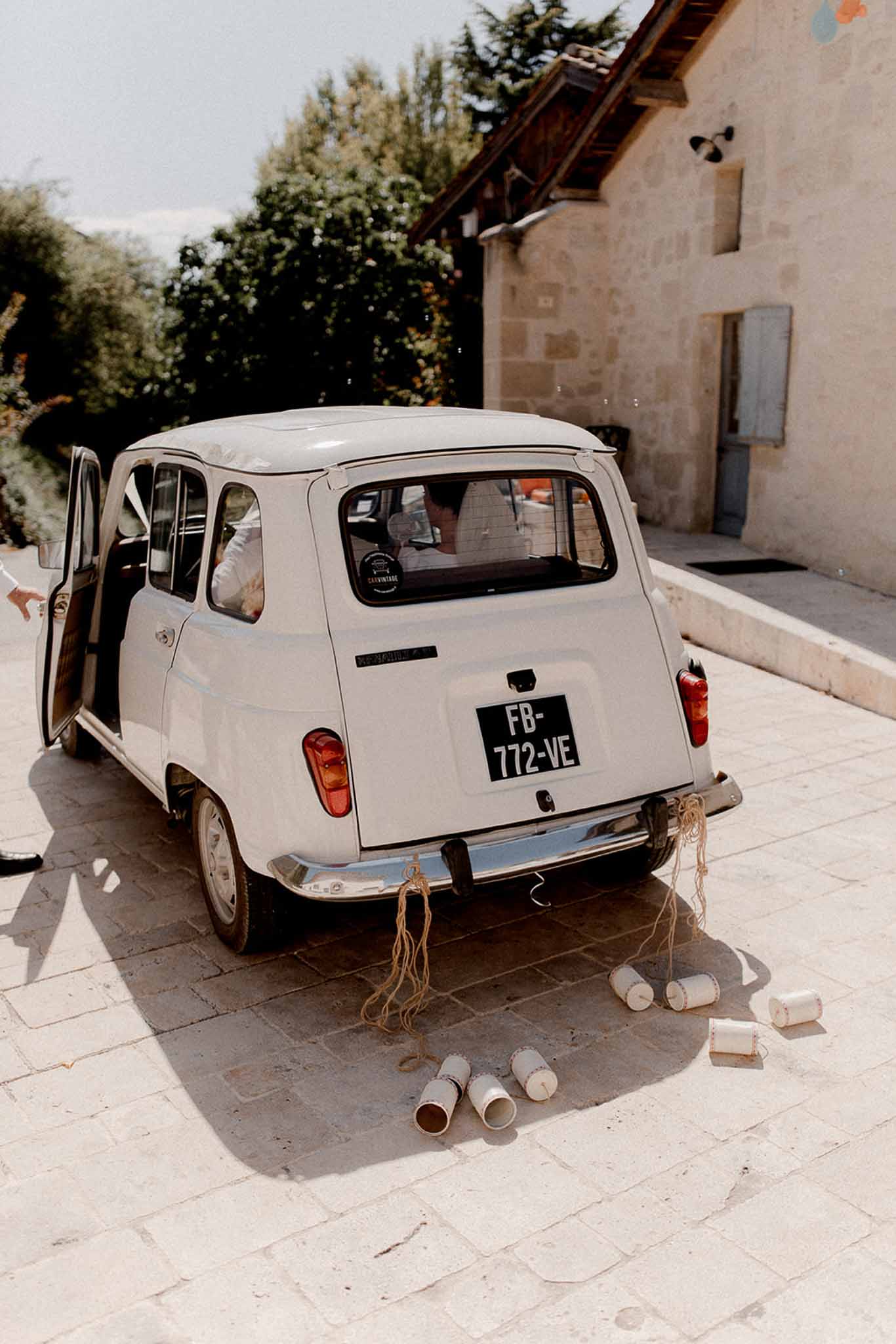 Vintage white Citroën decorated with tin cans for wedding departure at rustic stone courtyard