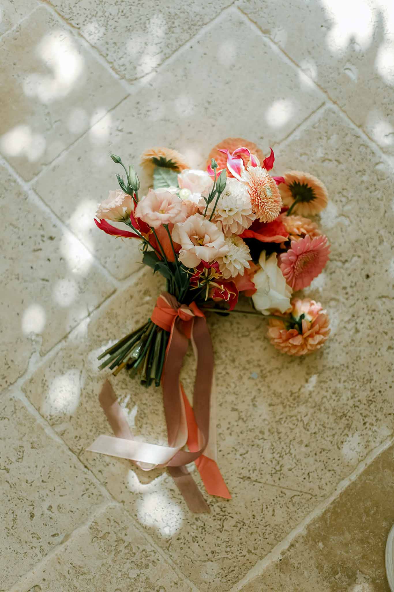 Bridal bouquet with cream dahlias and coral roses laid flat on stone tiles