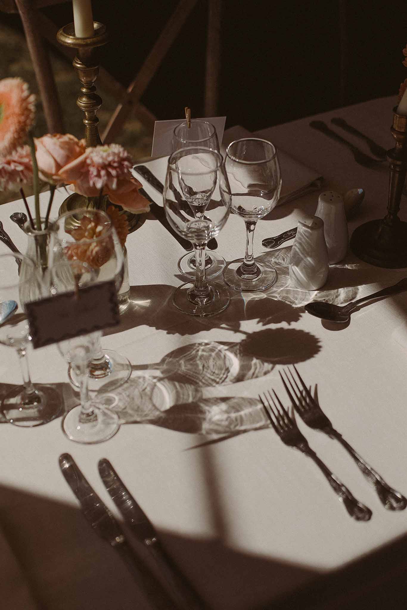 Reception table setting with peach dahlia centerpiece and brass candlesticks at outdoor evening wedding