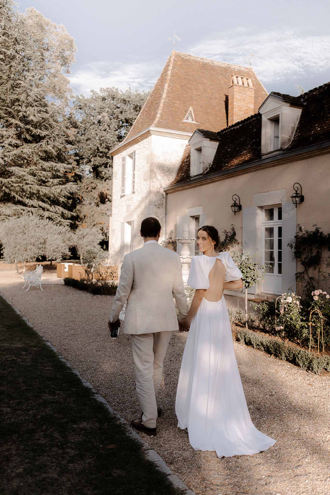 Bride and groom walking toward chapel with terracotta roof at estate wedding venue
