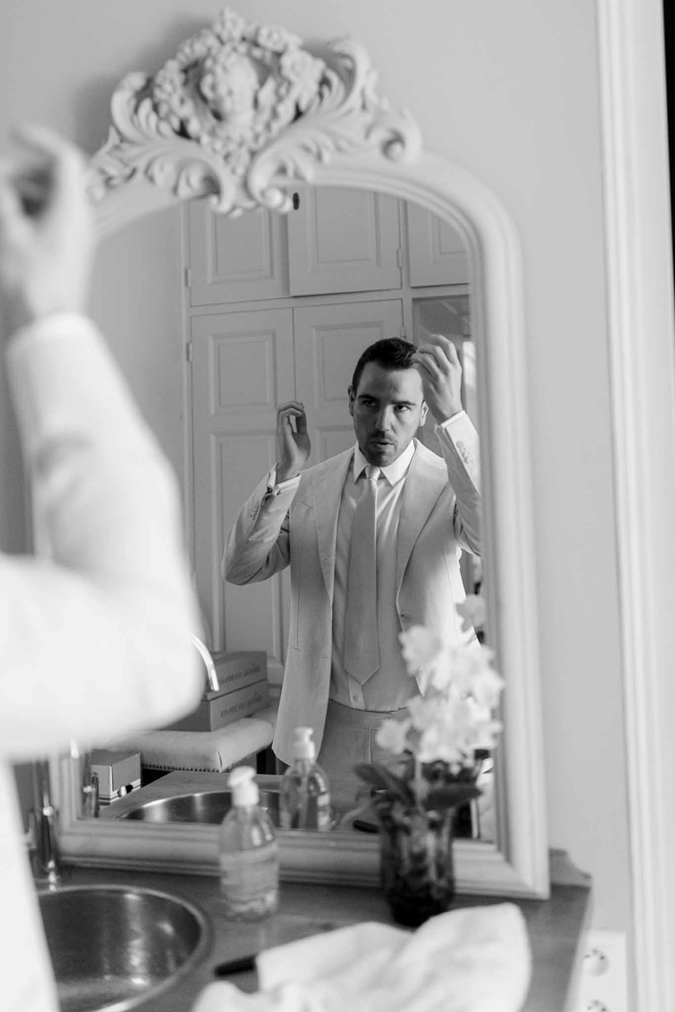 Groom adjusting hair in ornate bathroom mirror during wedding preparation at elegant venue