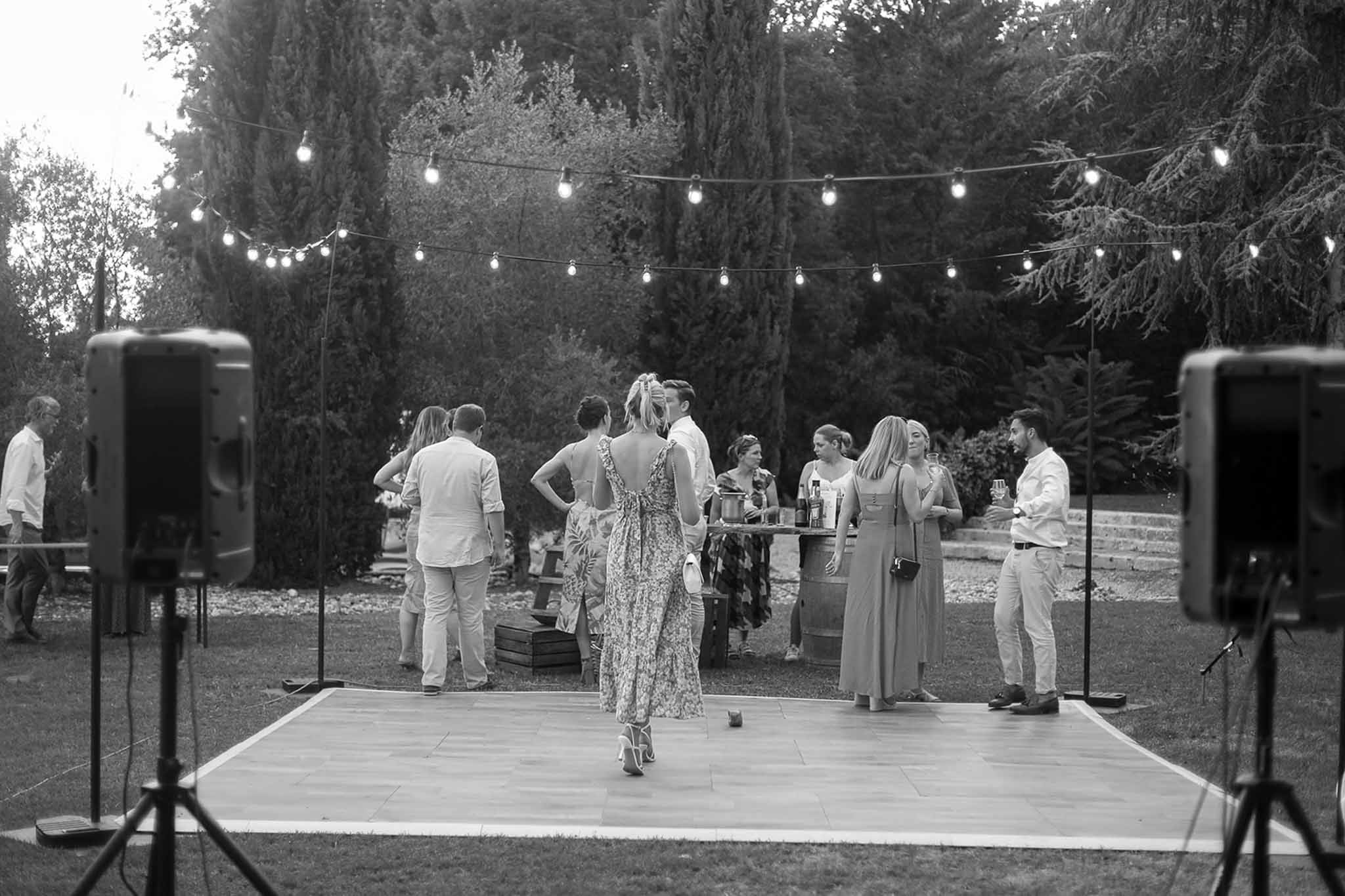 Wedding reception guests mingling and dancing on outdoor wooden dance floor in garden setting with string lights