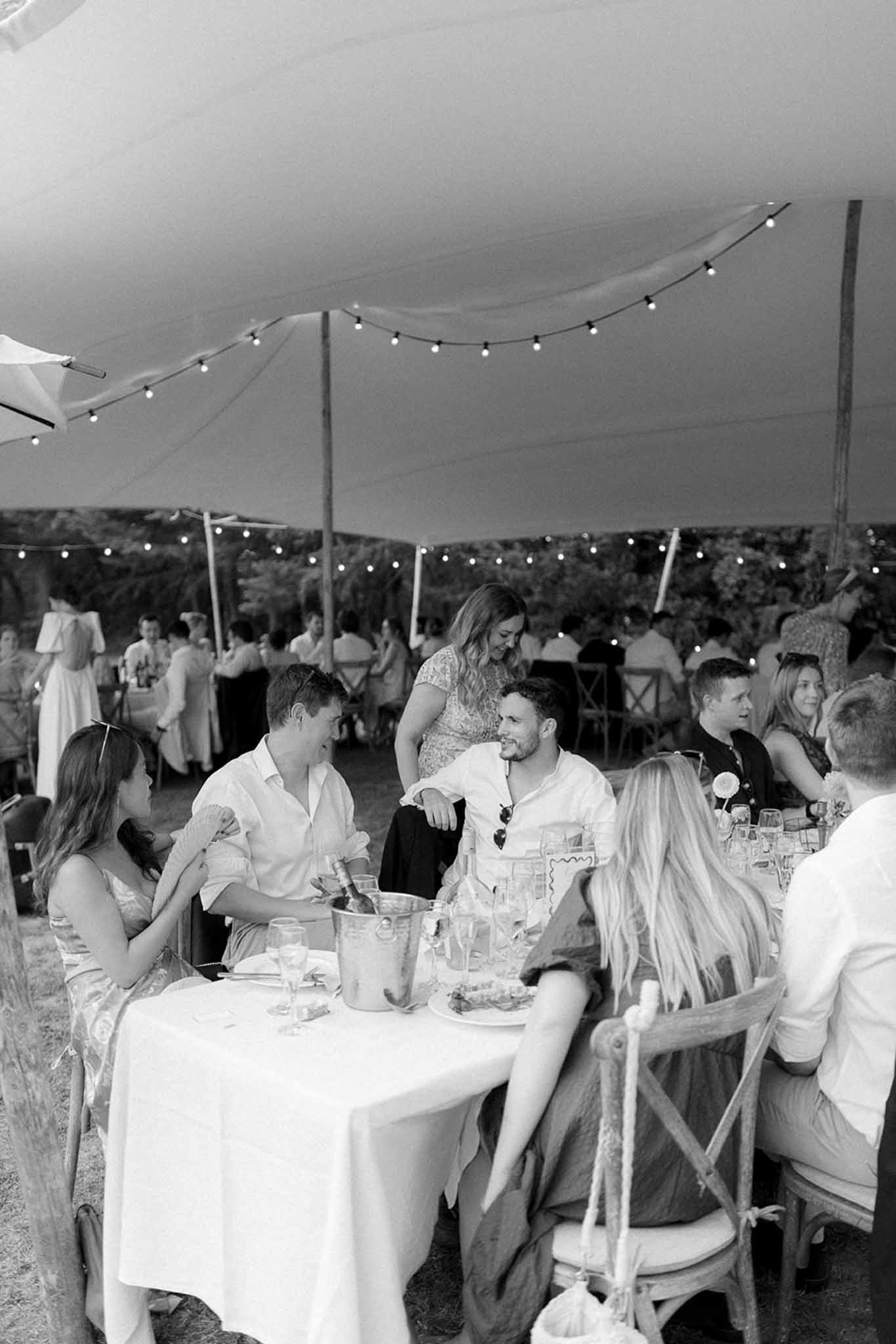 Wedding reception dinner under marquee tent with guests dining at round tables with string lights overhead