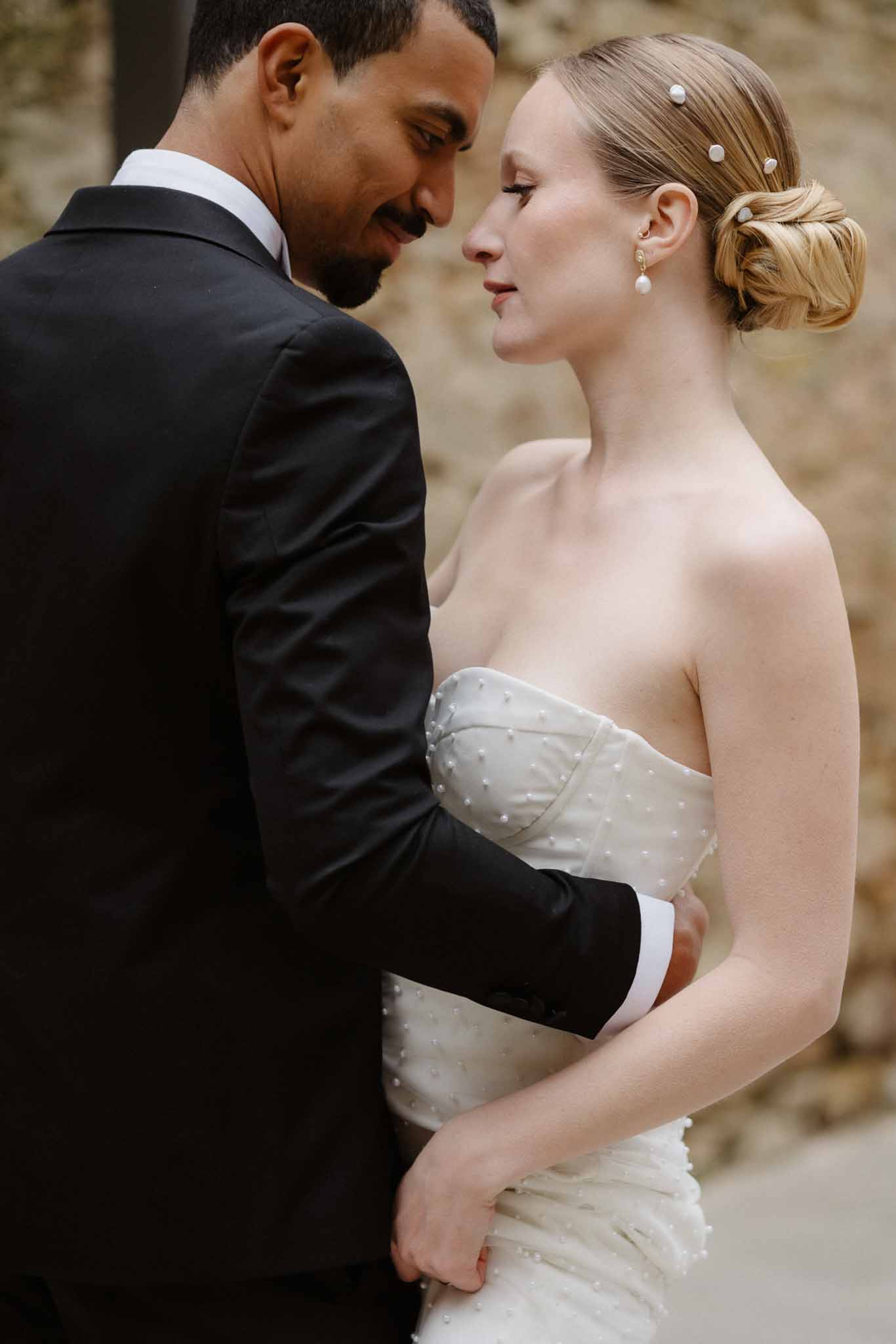 Intimate bride and groom portrait against stone wall showing classical wedding attire and pearl details