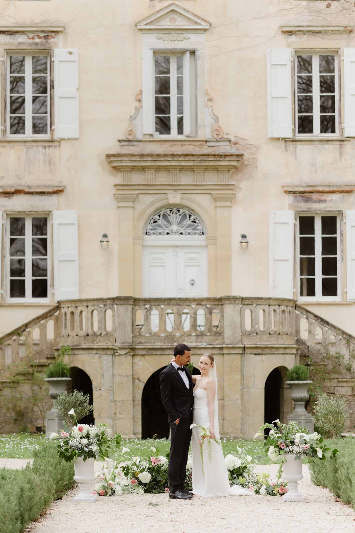 Bride and groom portrait in front of classical stone estate courtyard with formal floral arrangements
