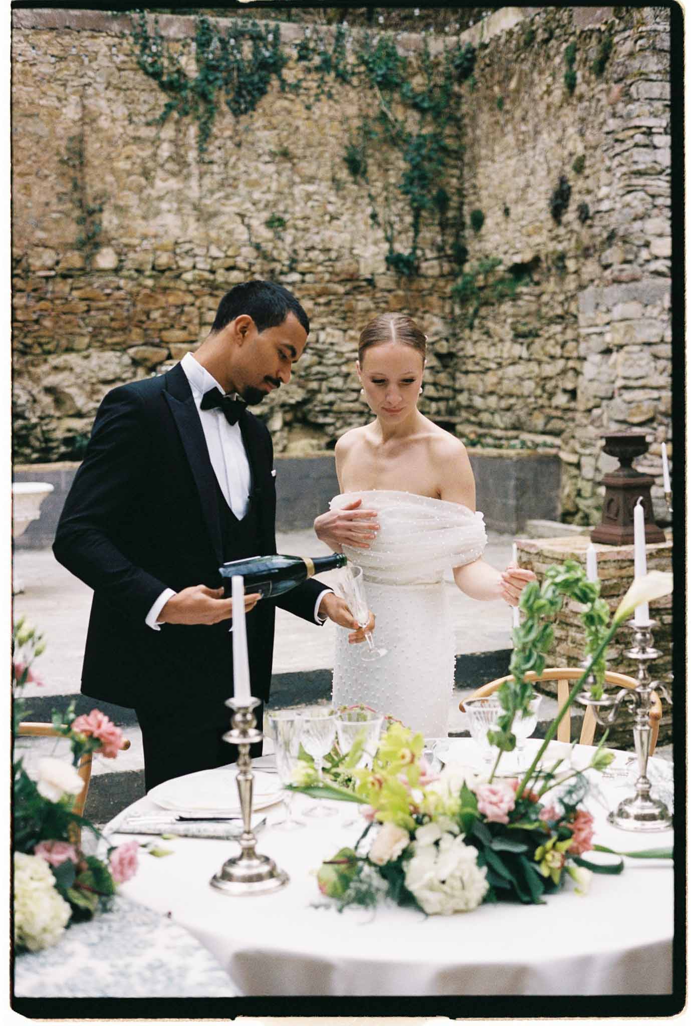 Bride and groom at reception table in historic stone courtyard with floral centerpieces
