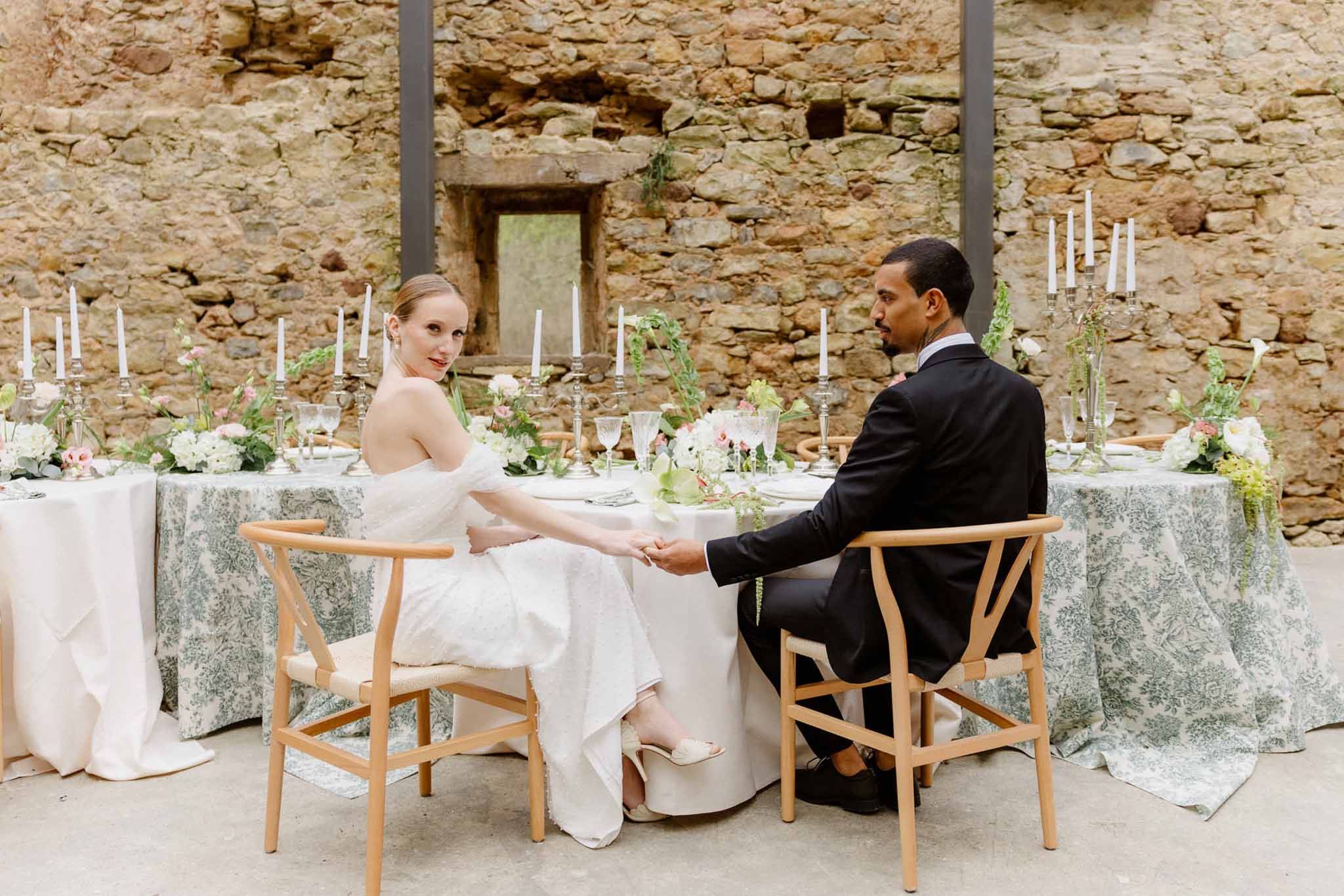 Bride and groom holding hands at reception table in stone courtyard setting