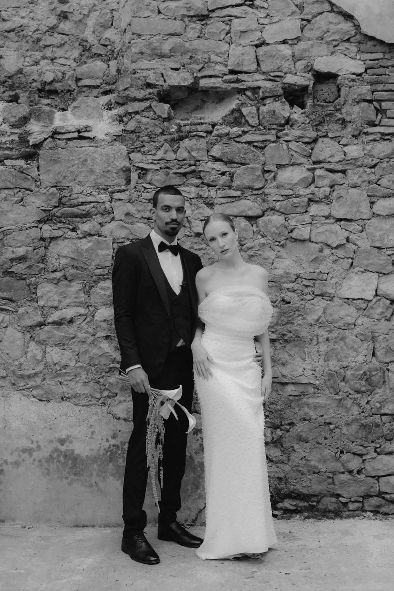 Bride and groom portrait against historic stone wall in black and white