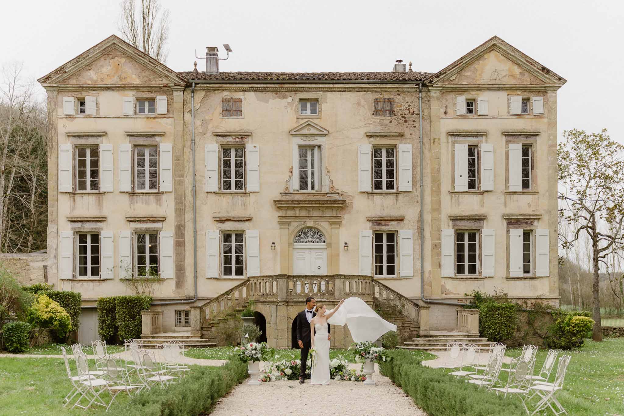 Outdoor wedding ceremony with bride and groom under white canopy at historic stone manor house