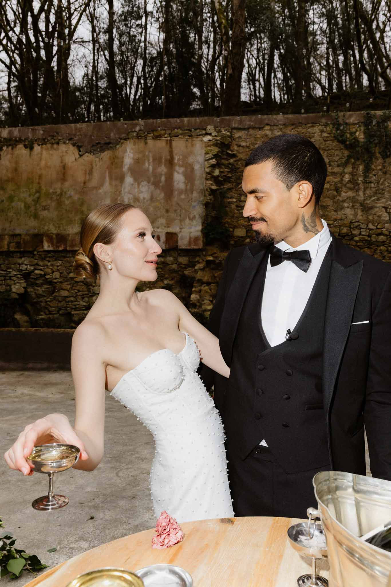 Bride and groom sharing champagne during cocktail hour in outdoor courtyard with stone wall backdrop