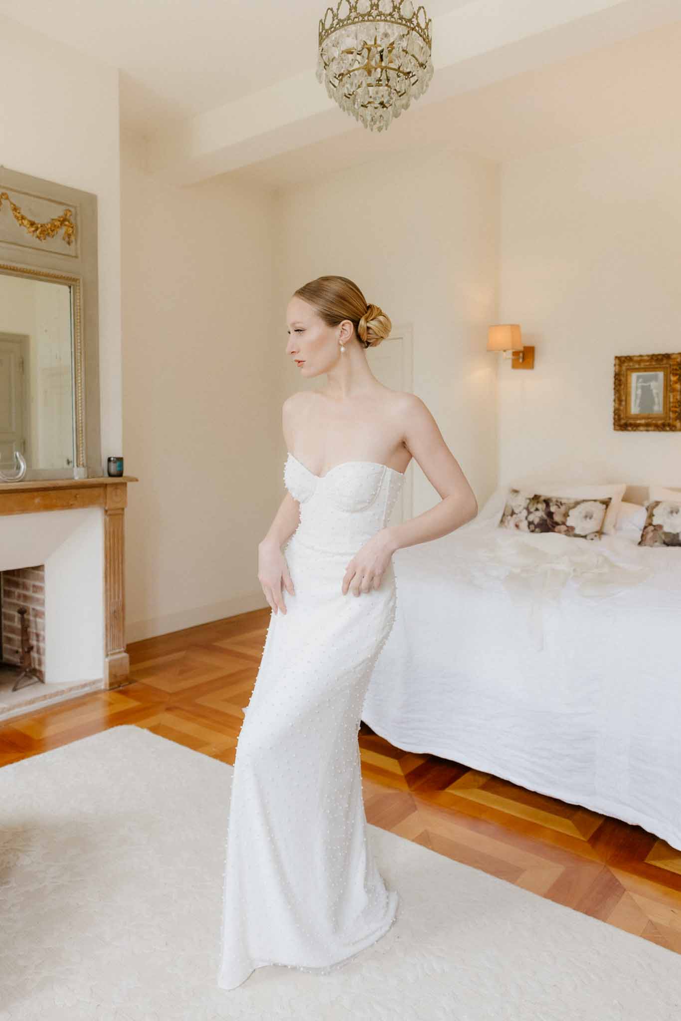 Bride in ivory beaded gown posing in elegant bedroom with crystal chandelier and classical decor