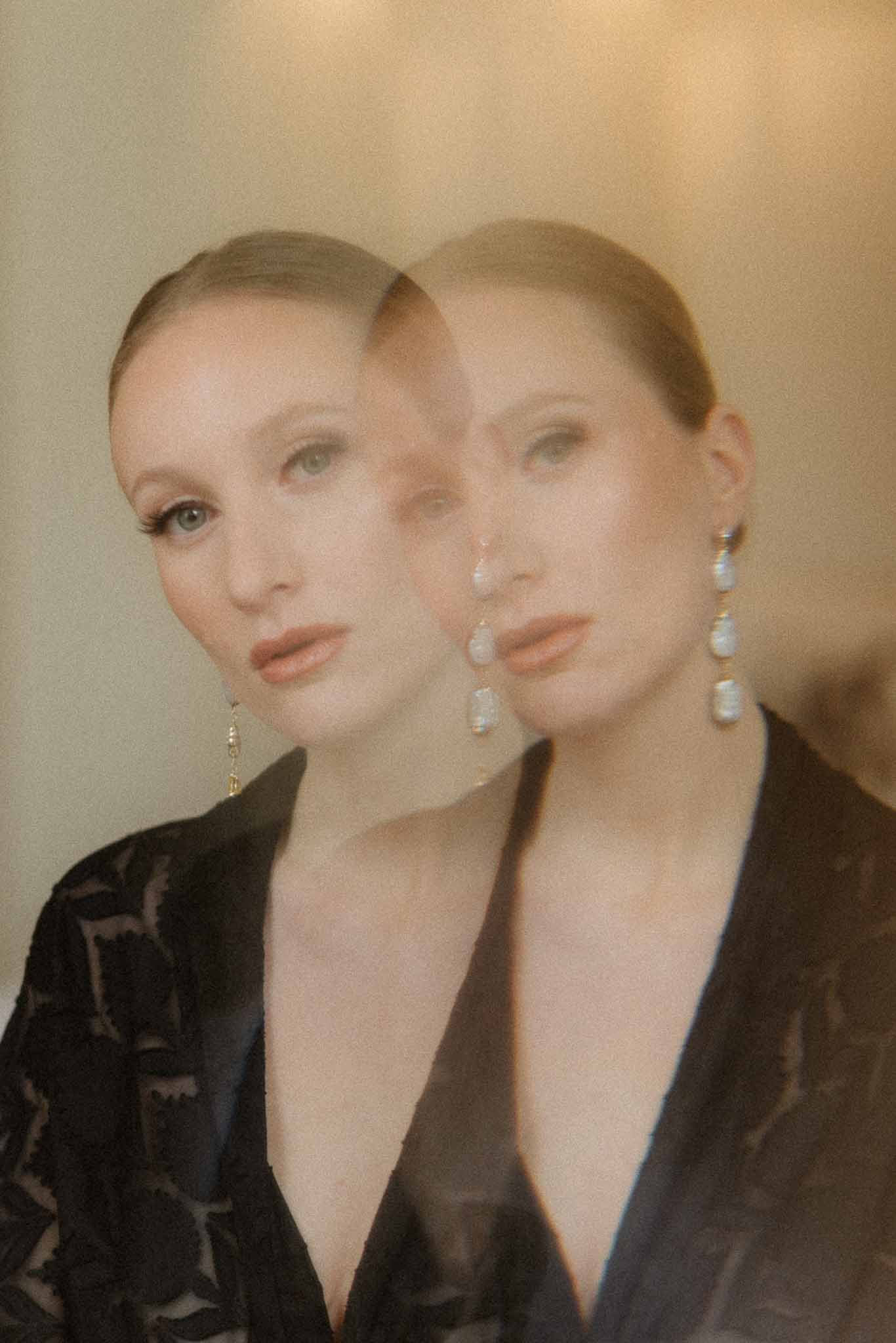 Two women in black clothing with pearl earrings against neutral studio background