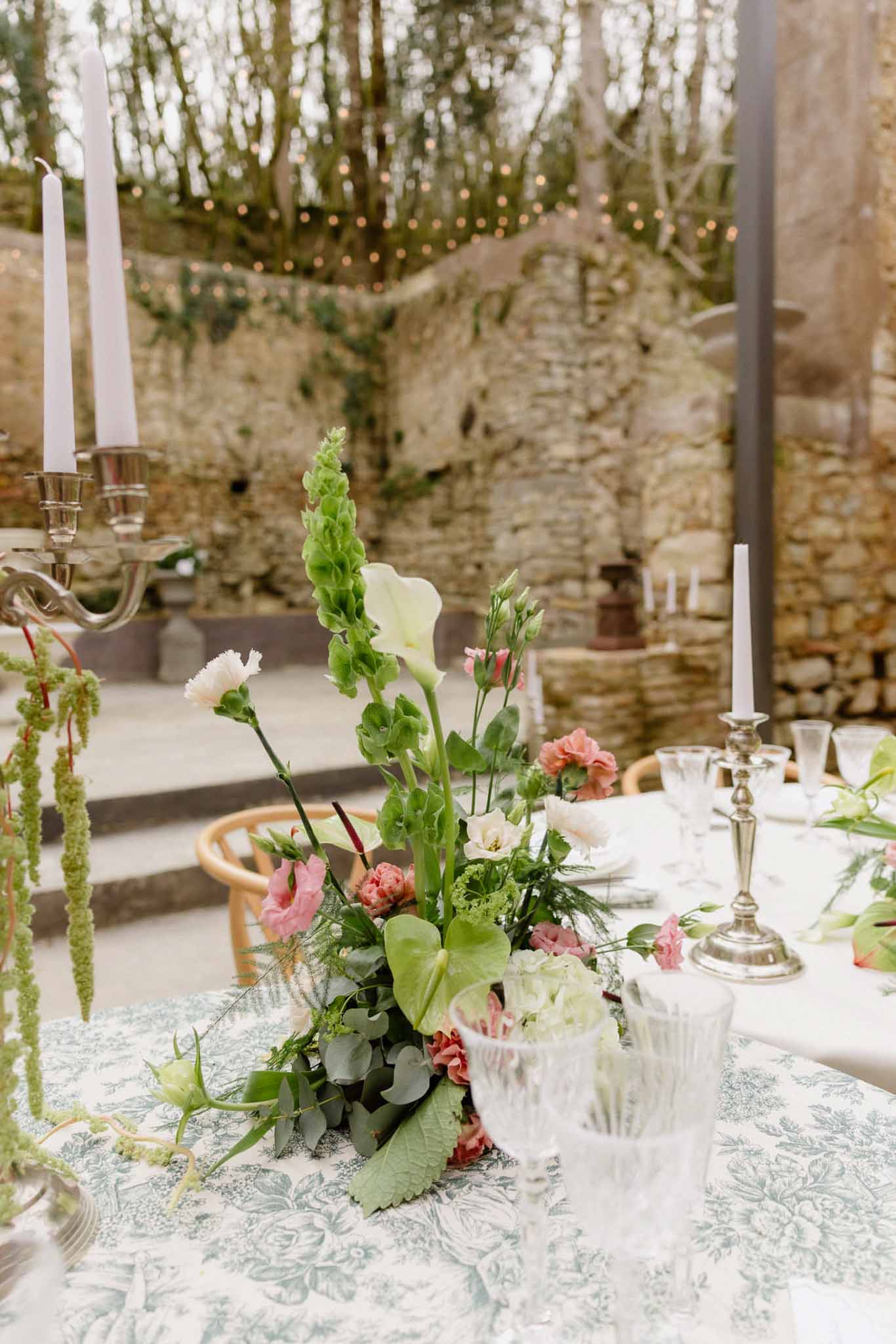 Reception table centerpiece with cream flowers and silver candelabras at outdoor stone courtyard venue