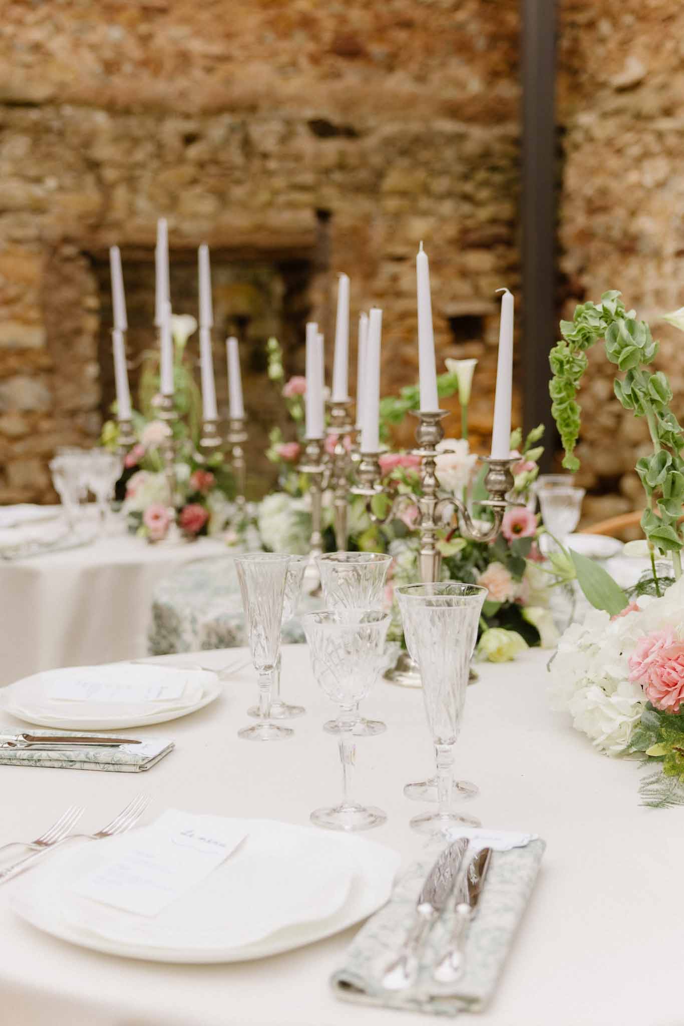 Wedding reception table setting with candelabra centerpiece at indoor stone courtyard venue