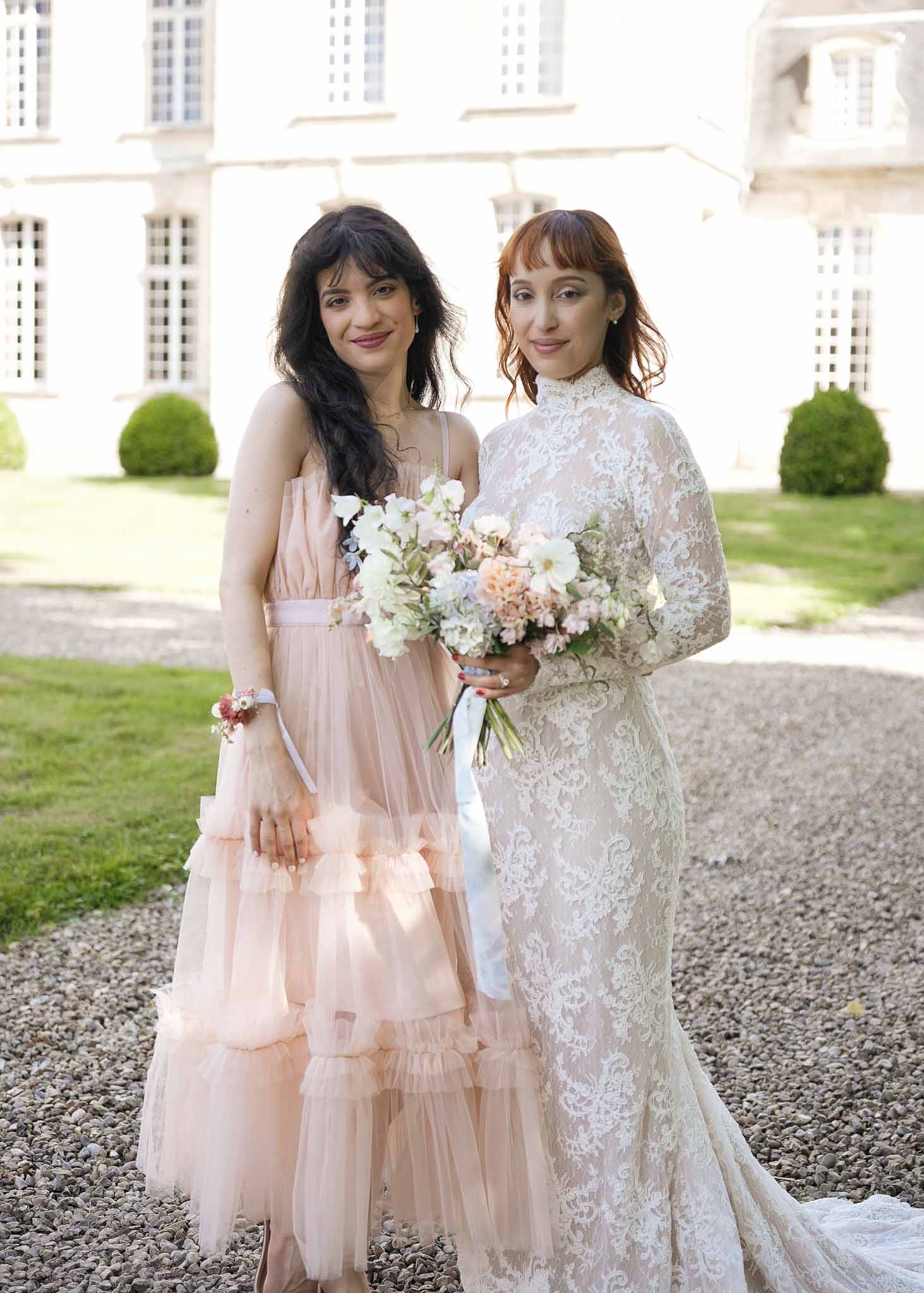 Bride and bridesmaid portrait in courtyard of classical stone mansion with manicured gardens