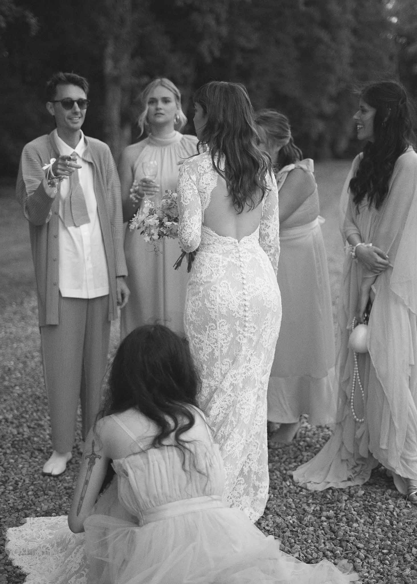 Bride surrounded by wedding guests in outdoor garden setting during reception