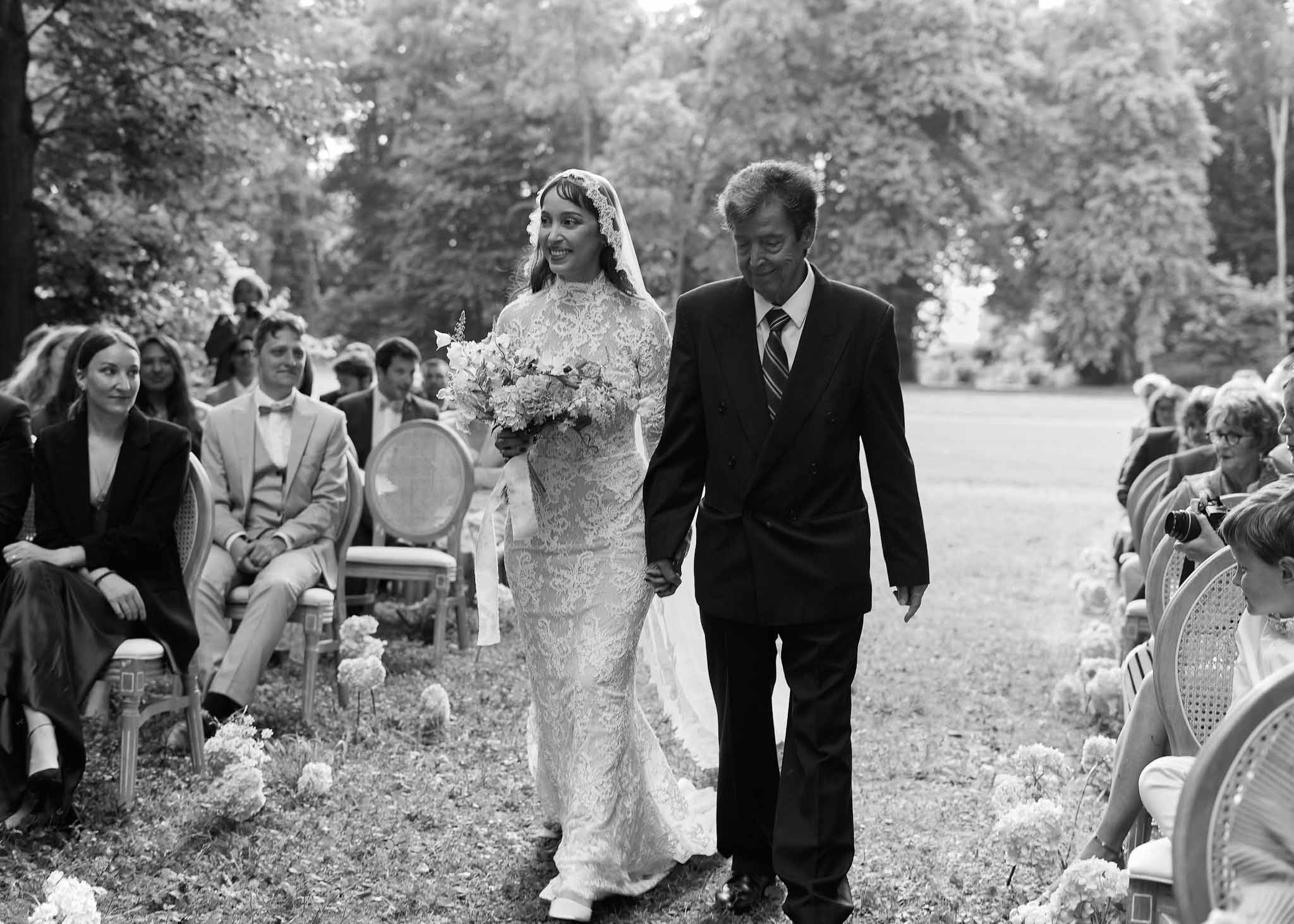 Bride and groom walking down aisle during outdoor garden wedding ceremony with guests seated in chairs