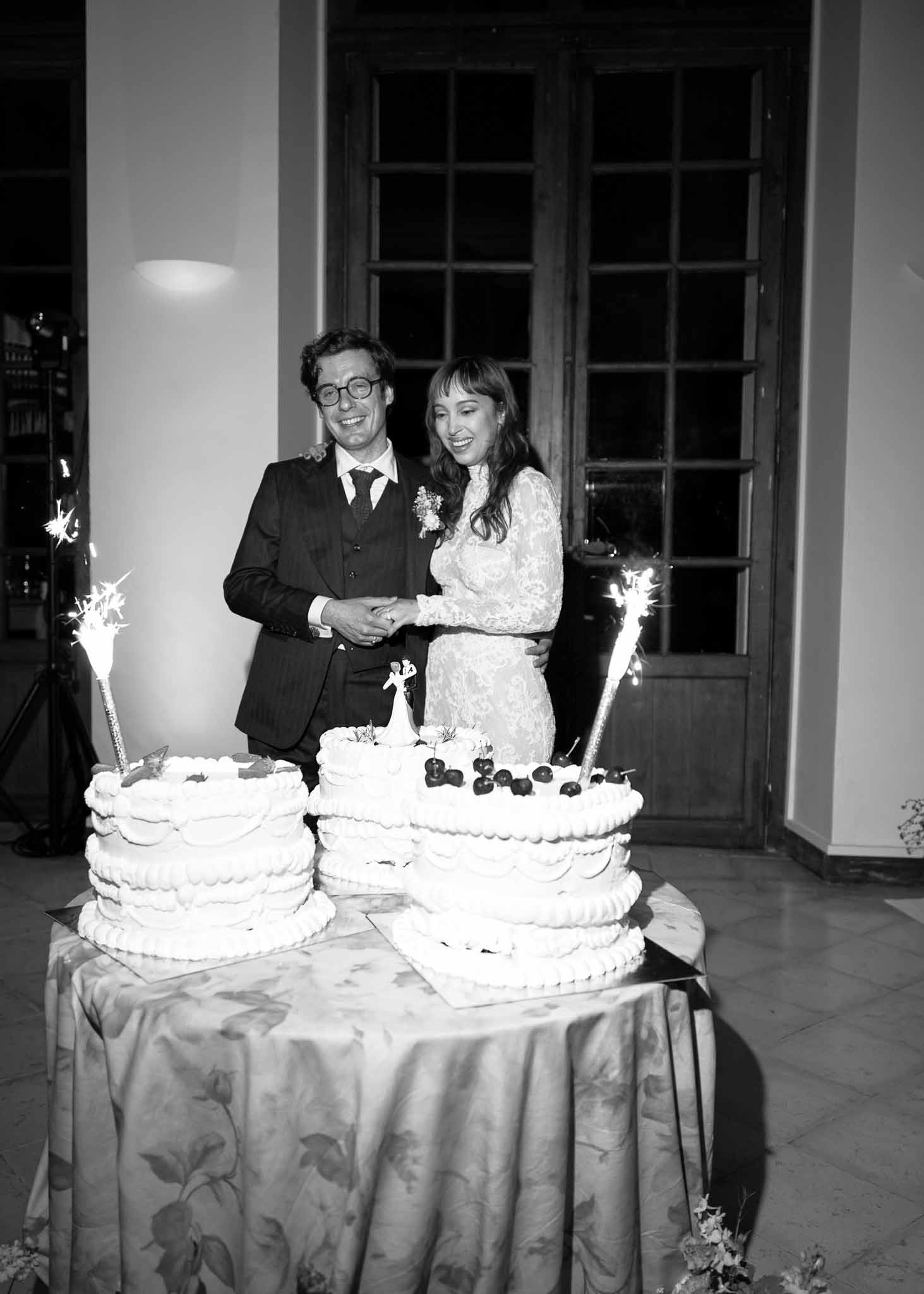 Bride and groom cutting wedding cake during indoor reception with sparklers and champagne