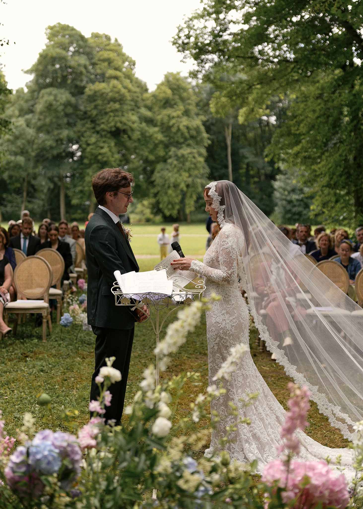 Bride and groom exchanging vows during outdoor garden ceremony with guests seated on lawn
