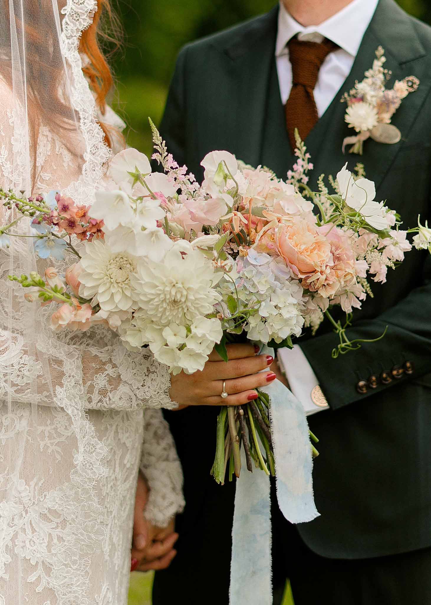 Bride and groom holding wedding bouquet during outdoor ceremony with ivory dahlias and peach roses