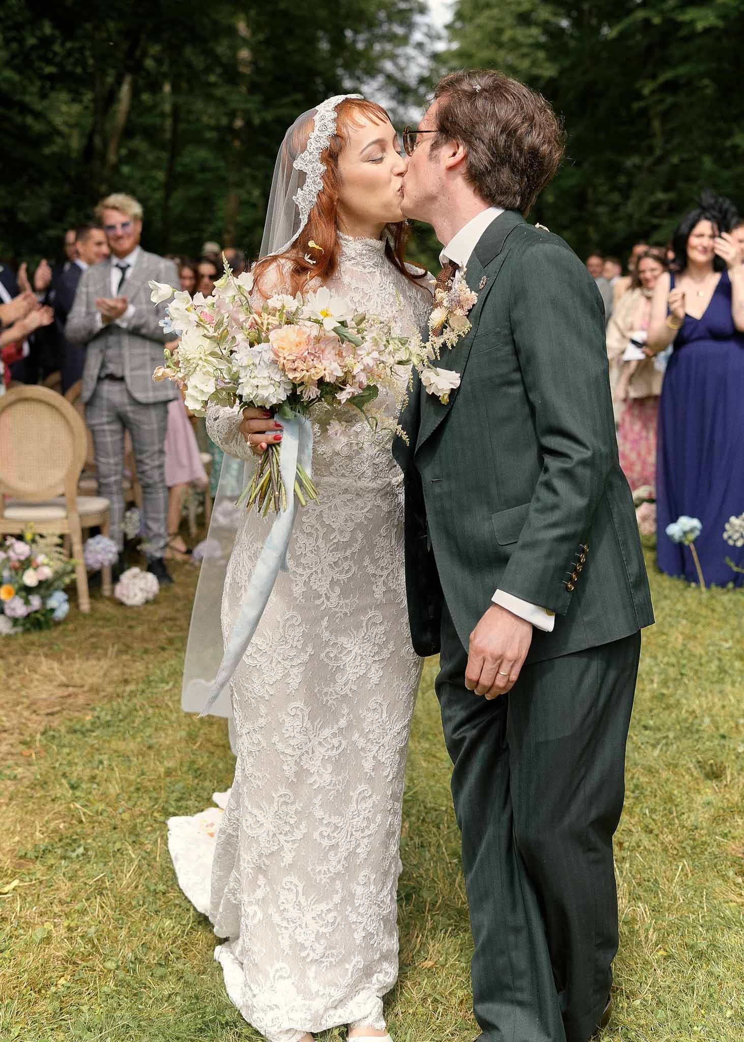 Bride and groom first kiss during outdoor garden wedding ceremony with guests applauding