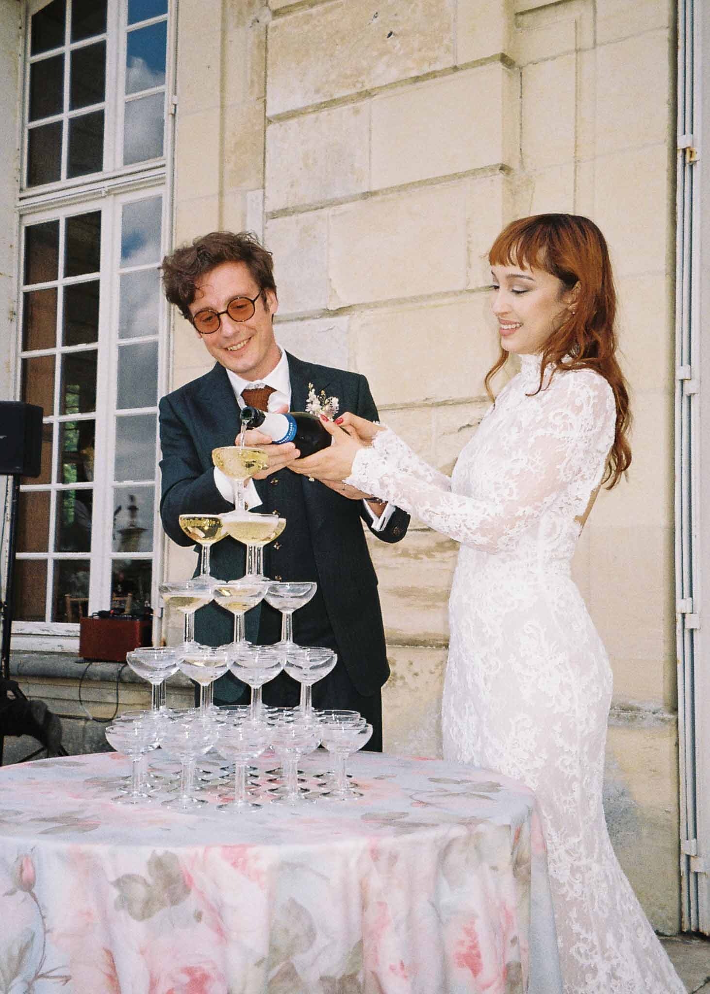 Bride and groom performing champagne tower toast during outdoor reception at stone courtyard venue
