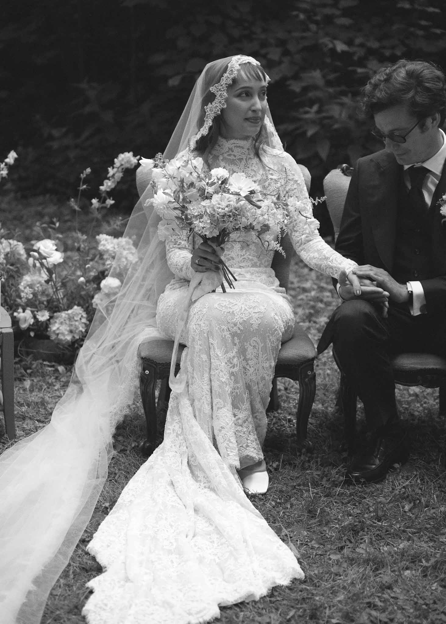 Bride and groom seated during outdoor garden ceremony in black and white