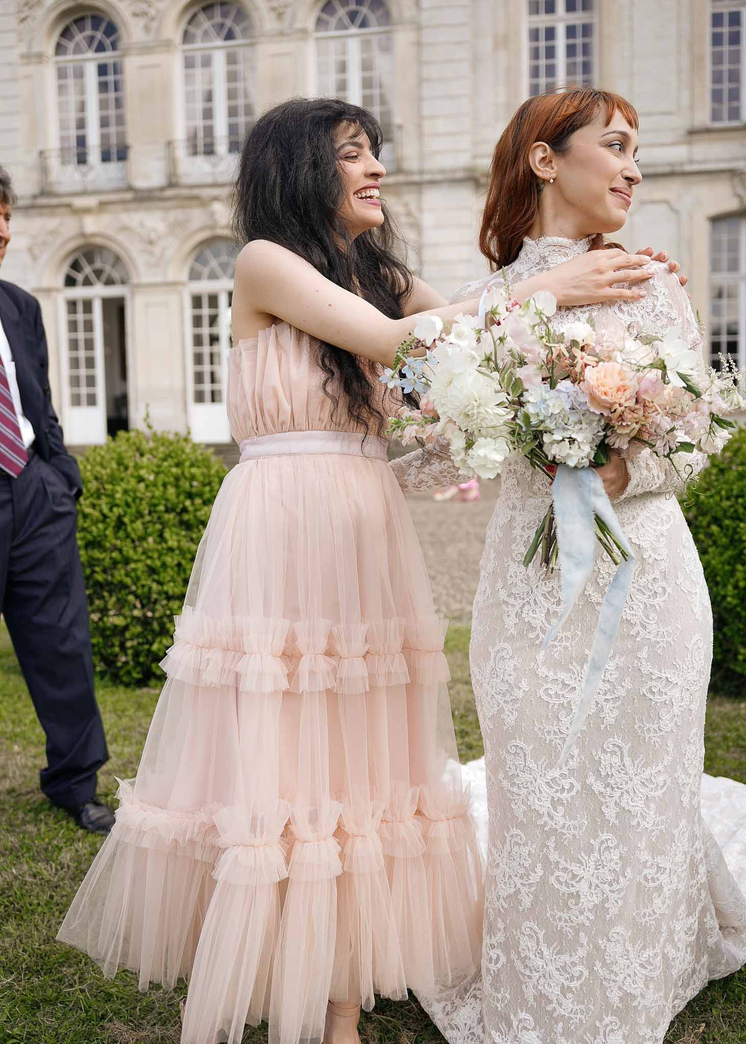 Bride and bridesmaid posing together in garden at classical stone venue