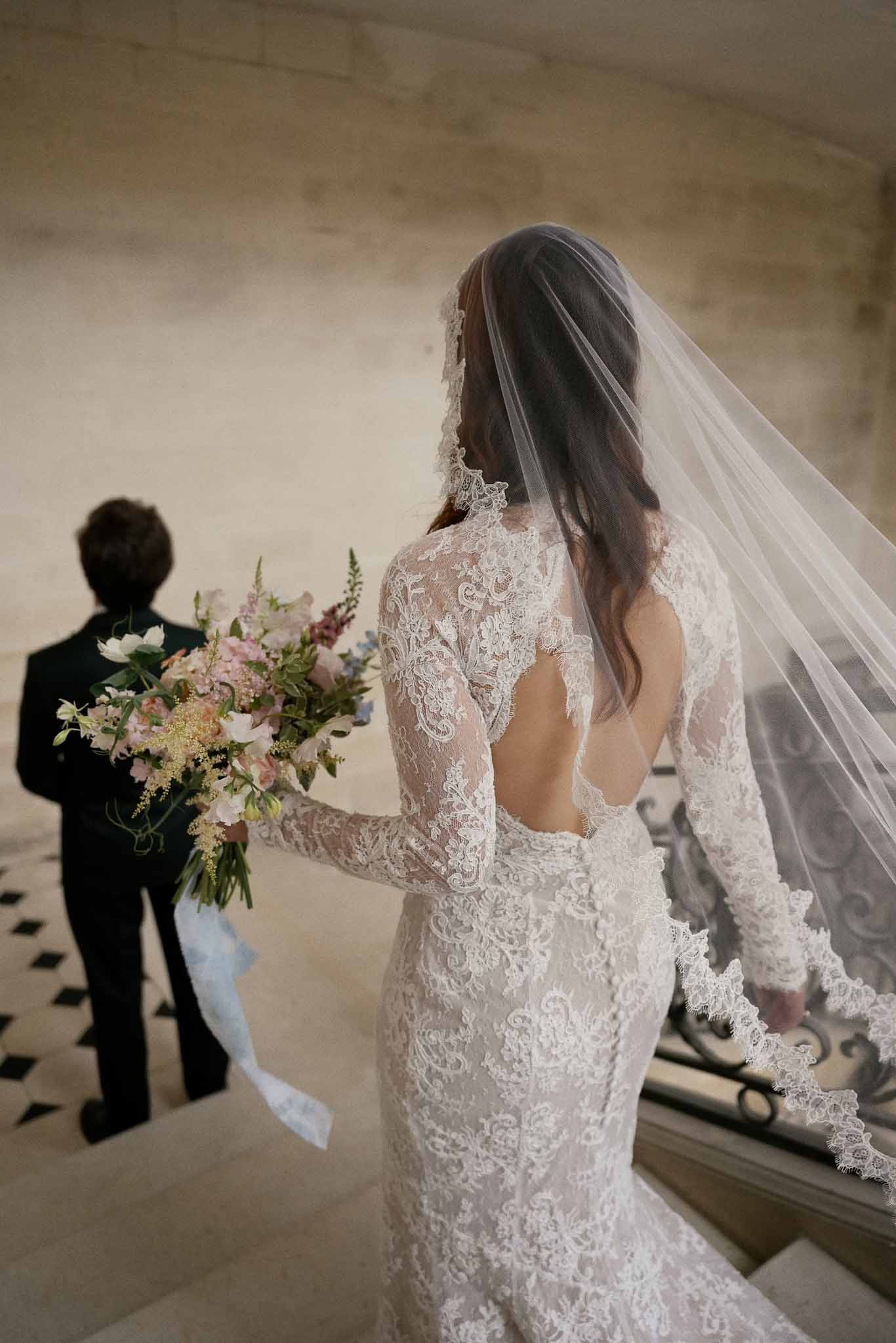 Bride in ivory lace dress with open back detail and veil at indoor venue with stone walls