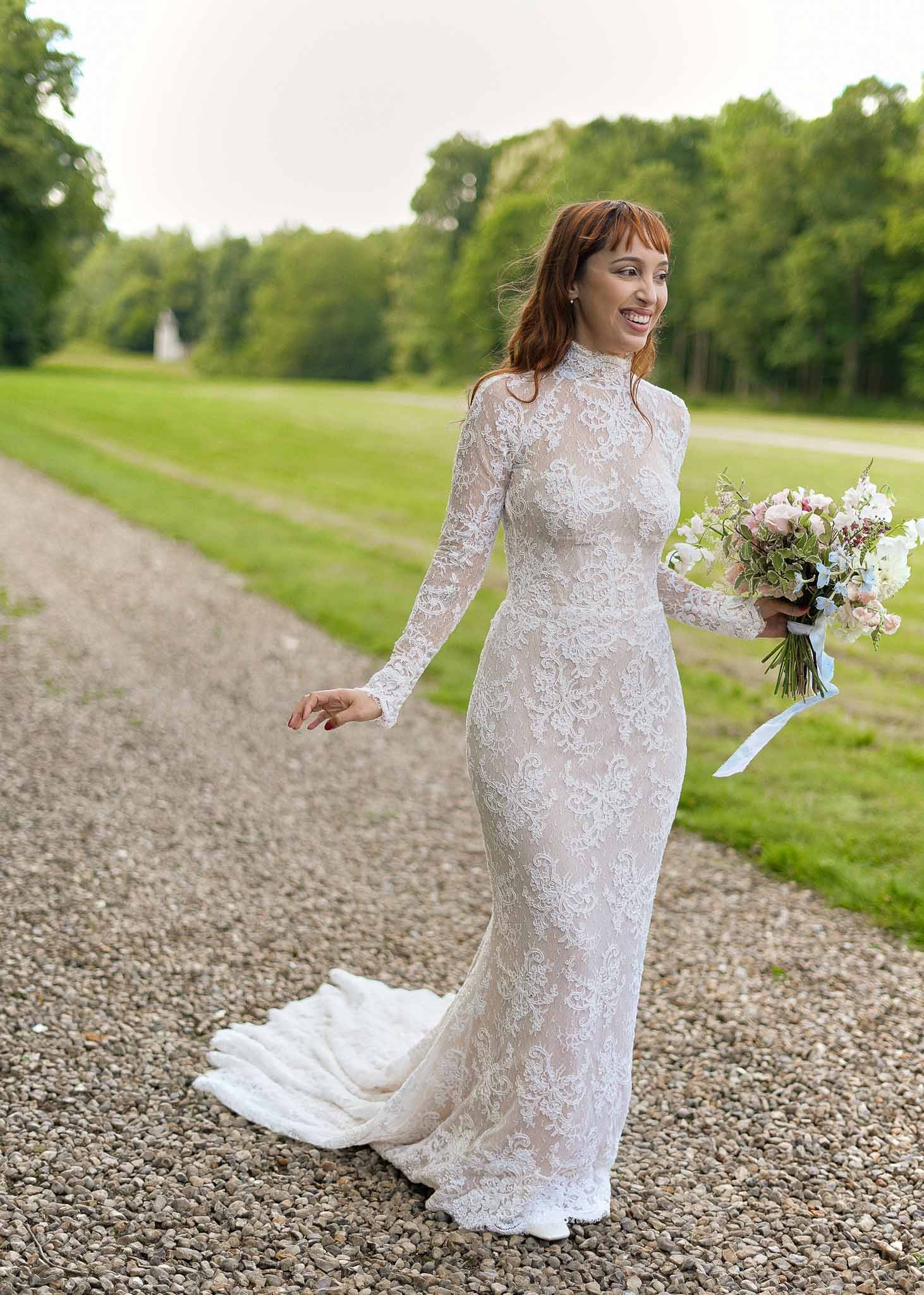Bride in ivory lace wedding dress holding white bouquet on estate grounds