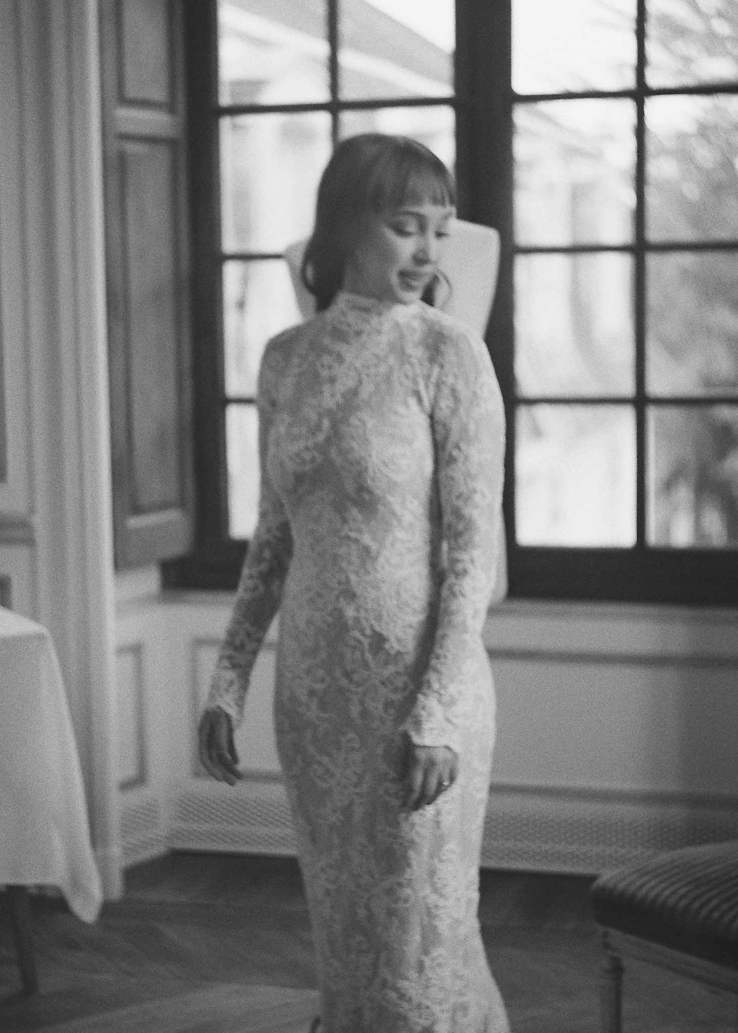 Bride in beaded wedding gown standing by large windows in elegant interior space