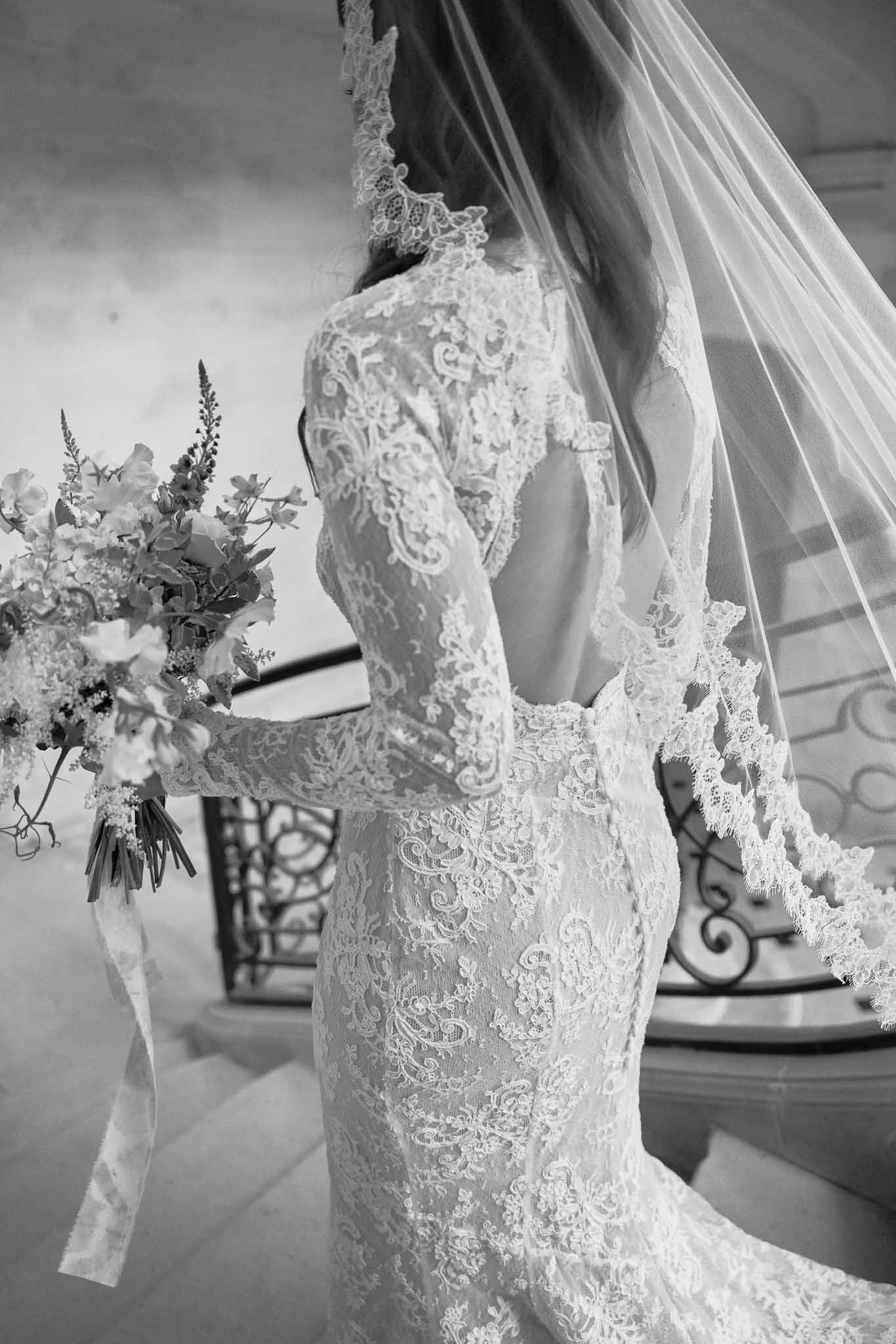Bride's hands holding white bouquet with lace dress and veil detail at elegant indoor venue