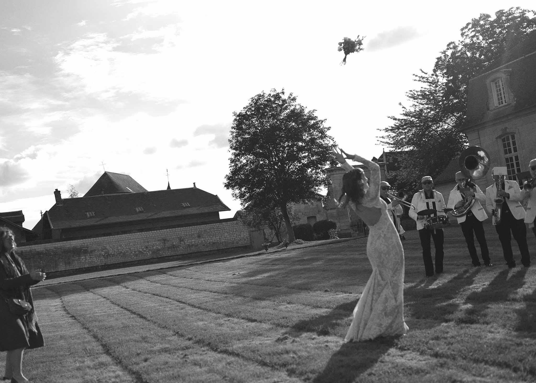 Bouquet toss moment in historic stone courtyard with wedding guests and musicians