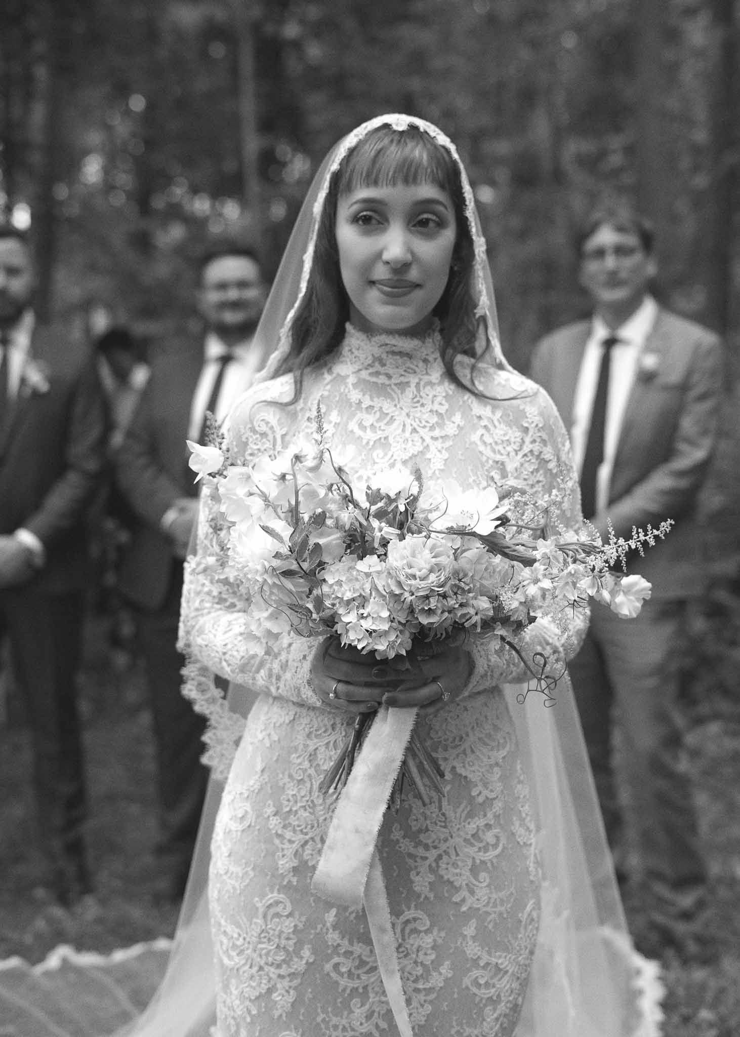 Bride in lace gown holding peony bouquet at outdoor garden ceremony