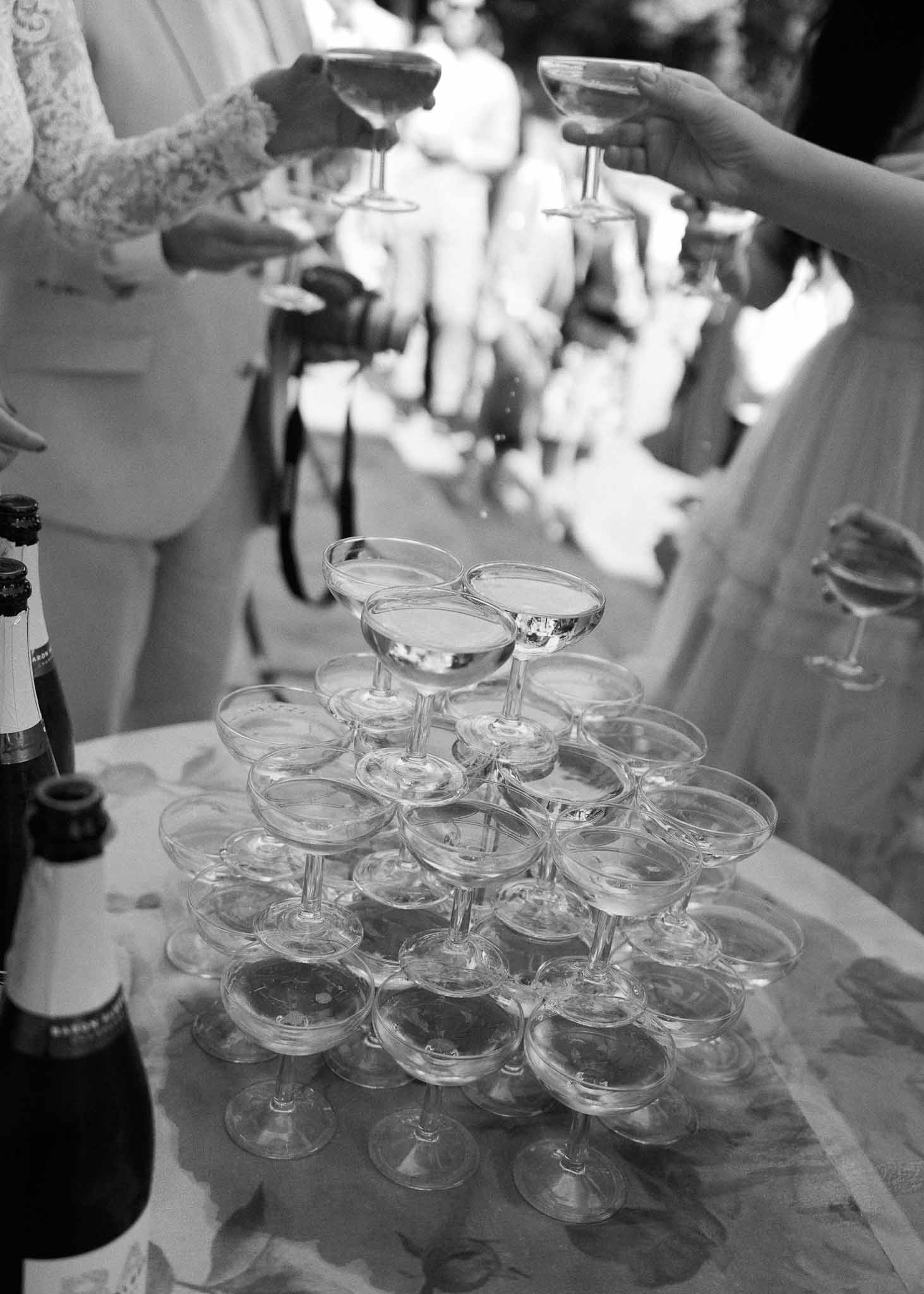Champagne tower with guests reaching for glasses during wedding reception