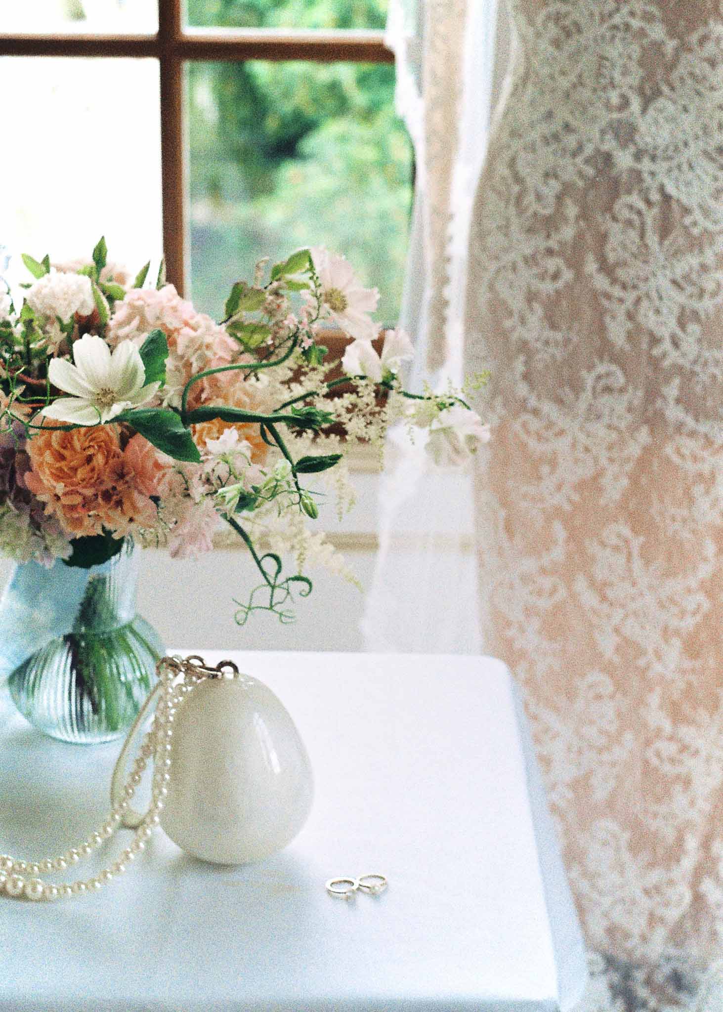 Bridal flat lay with bouquet, rings, and pearl ornament on windowsill in interior room