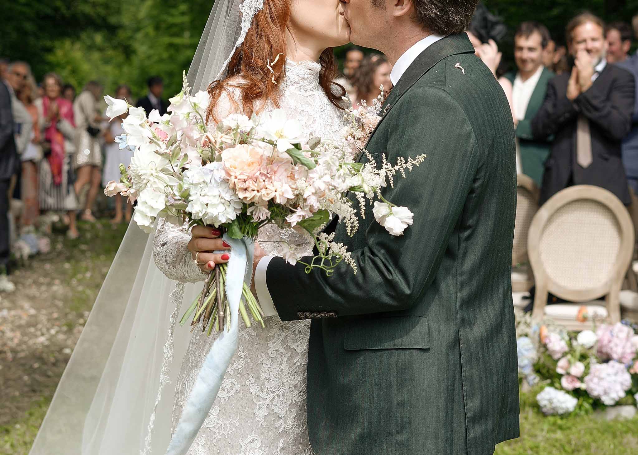 Bride and groom first kiss during outdoor garden ceremony with floral aisle arrangements