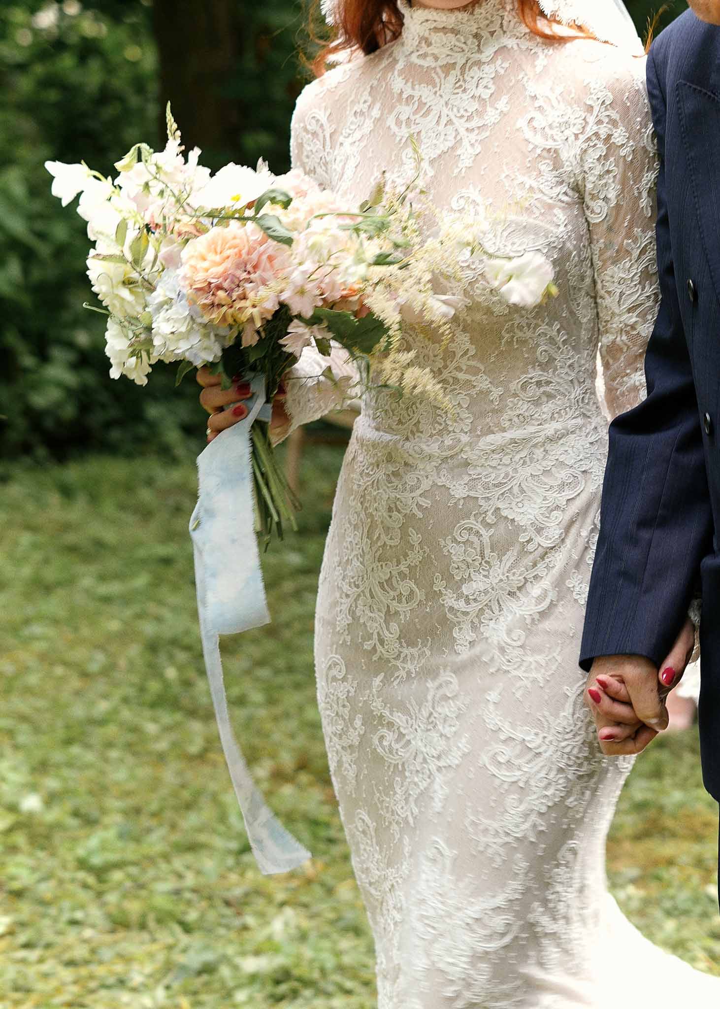 Bride and groom holding hands during outdoor garden ceremony with bouquet