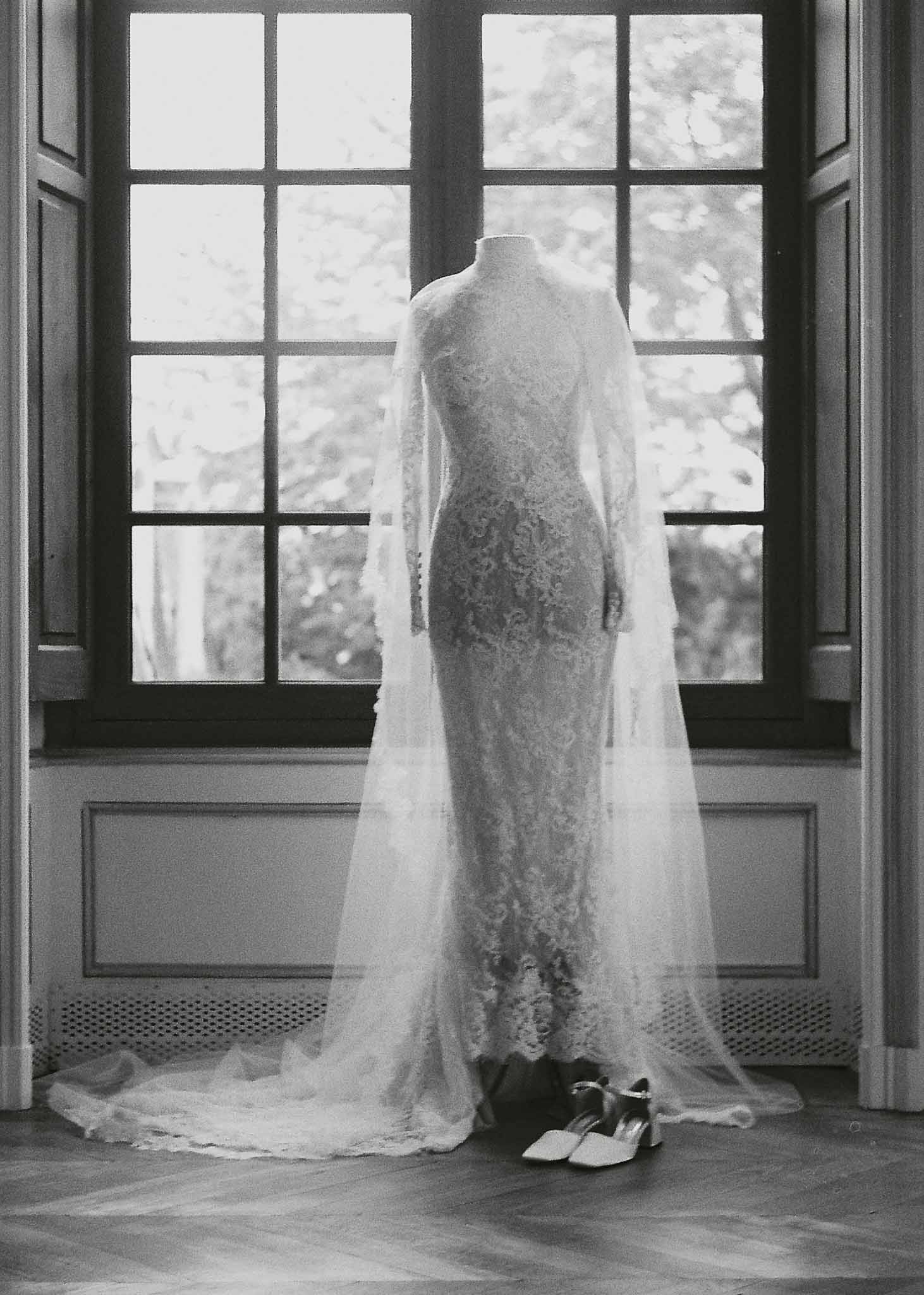 Bride in lace wedding dress and veil during getting ready moment at interior venue with tall windows