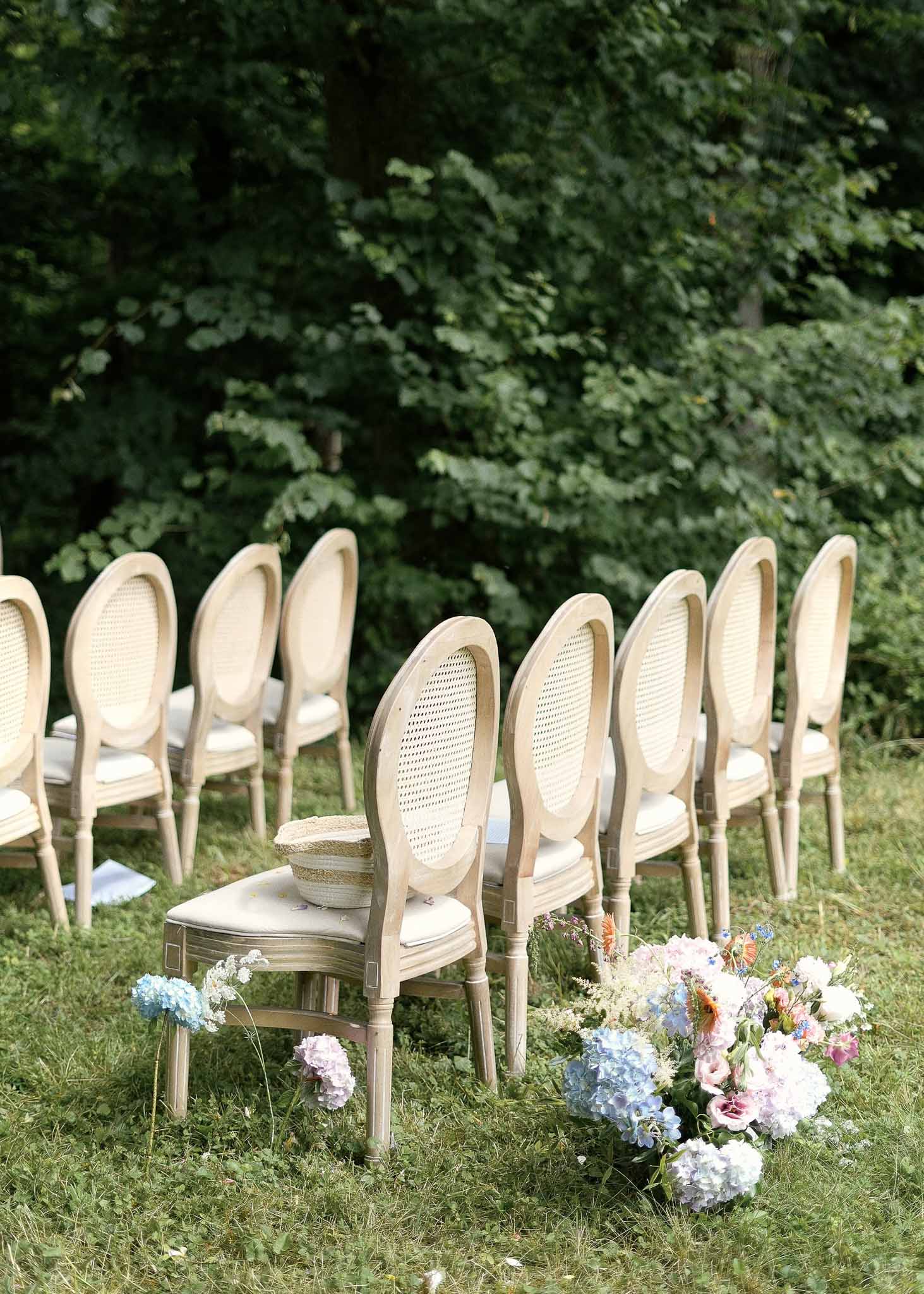 Outdoor wedding ceremony setup with wooden chairs and floral aisle arrangements in garden setting