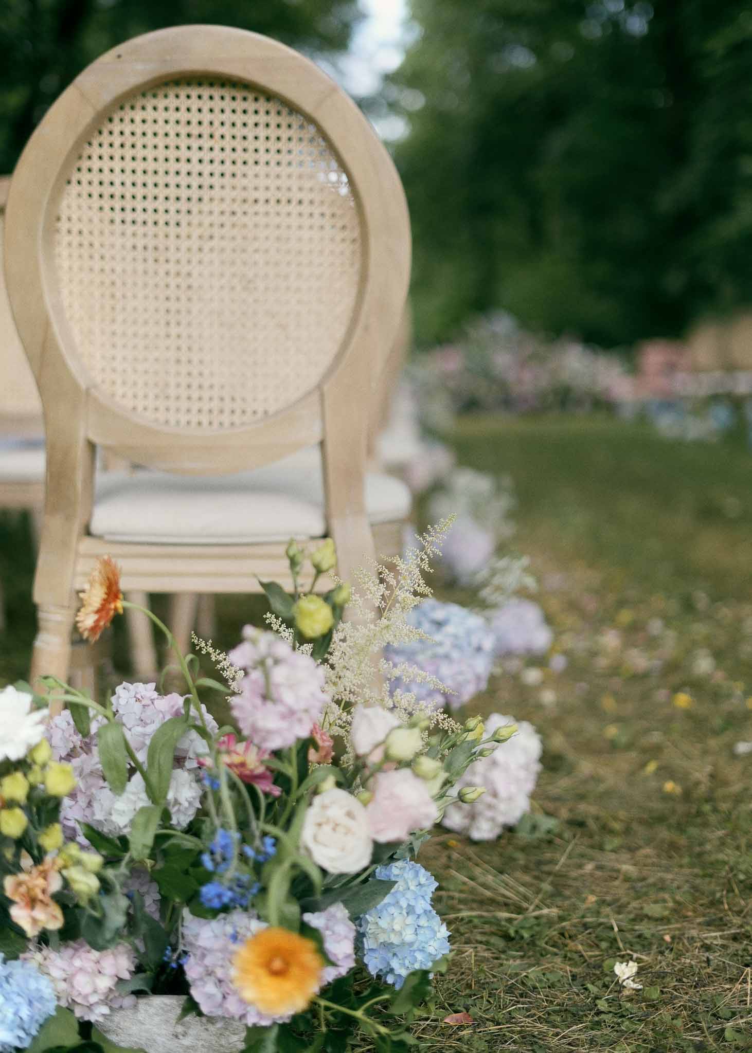 Cream rattan ceremony chair with mixed floral arrangement at garden wedding venue