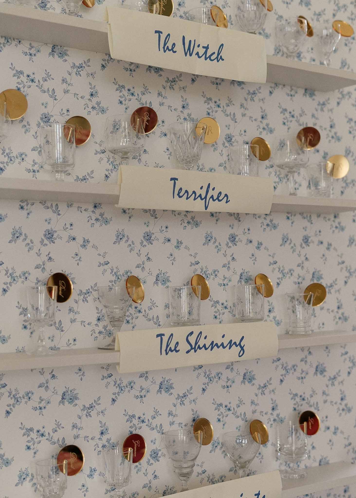 Horror-themed seating chart display with labeled shelves and glassware at wedding reception