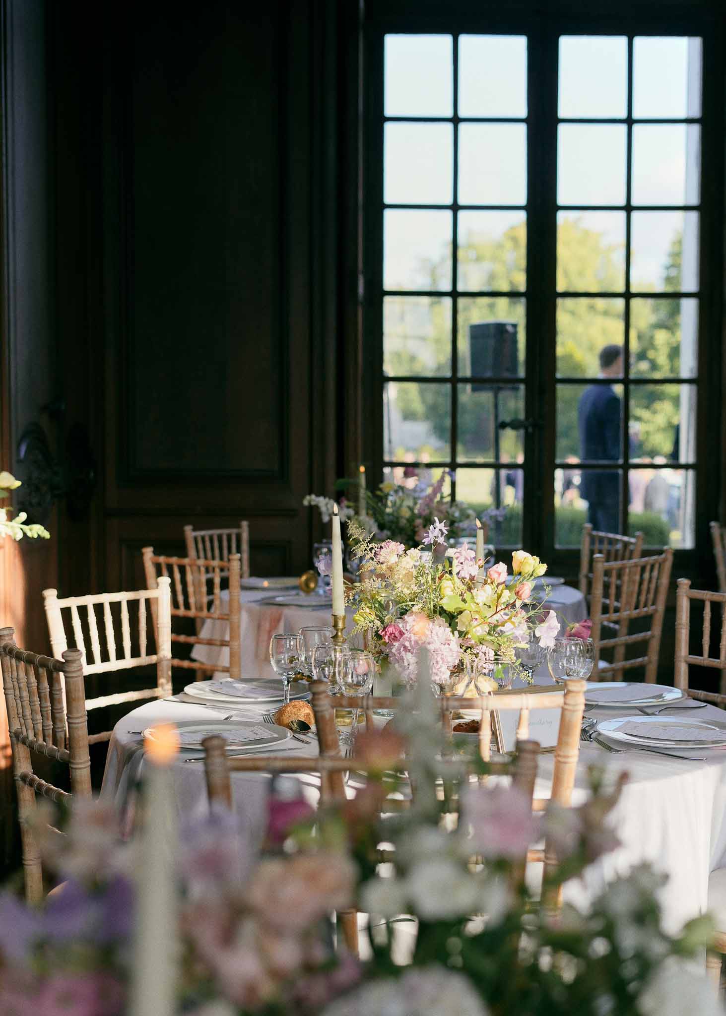 Reception table setting with floral centerpieces in elegant indoor dining room with garden views