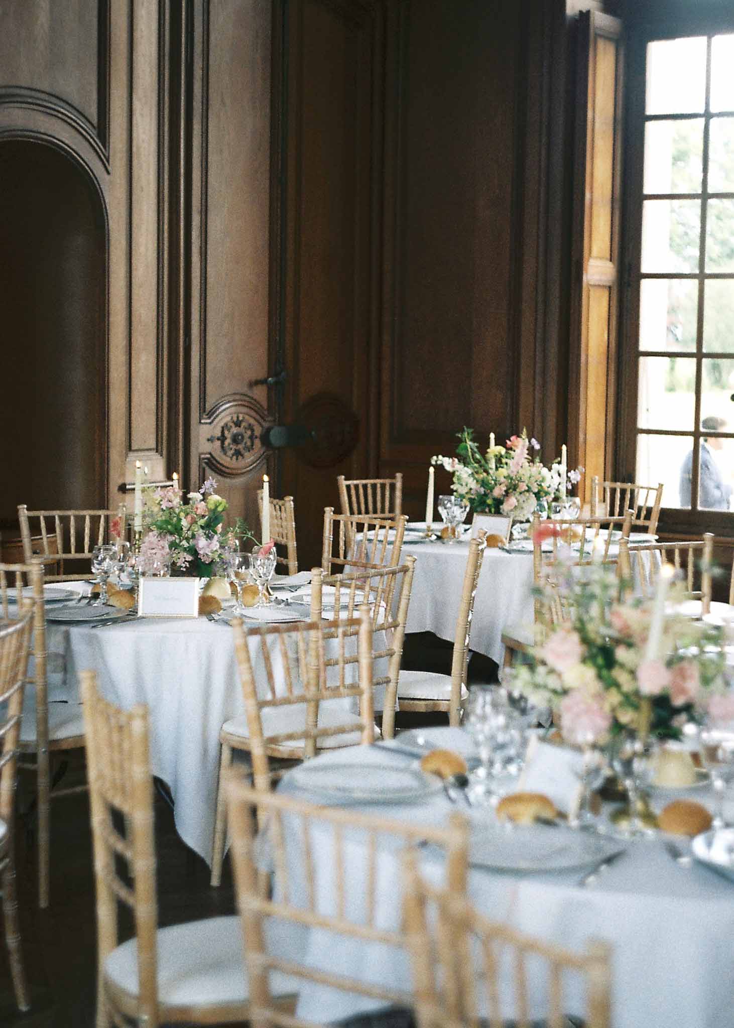 Reception dining setup with floral centerpieces in elegant ballroom with dark wood paneling