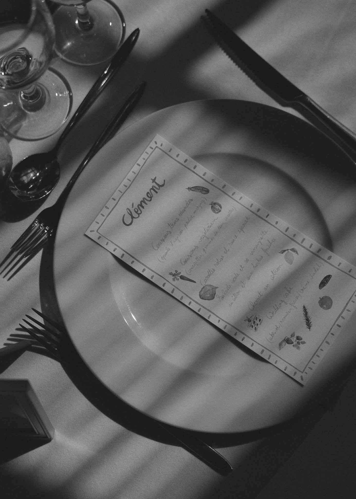Black and white close-up of formal place setting with botanical menu card and black flatware at wedding reception